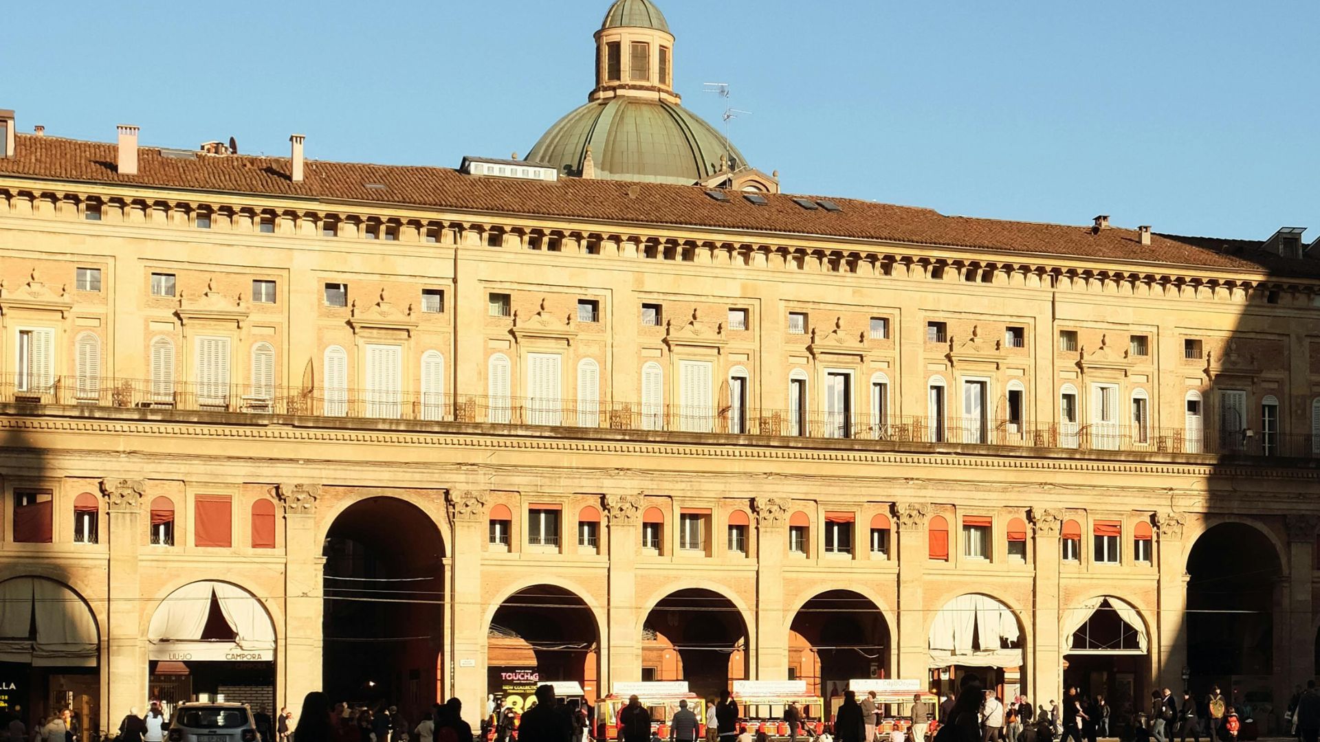 The image shows the Palazzo dei Banchi, in Bologna, Italy,  The Palazzo dei Banchi is characterized by its portico with arches at ground level and its upper floors with windows and decorative elements.