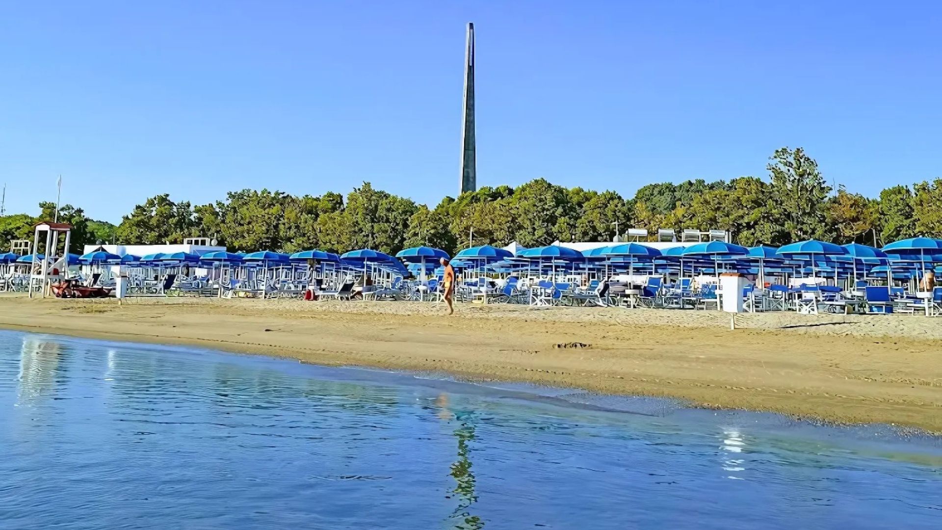 Image shows beach umbrellas, tables, chairs, and people on a beach in Pescara, Italy.