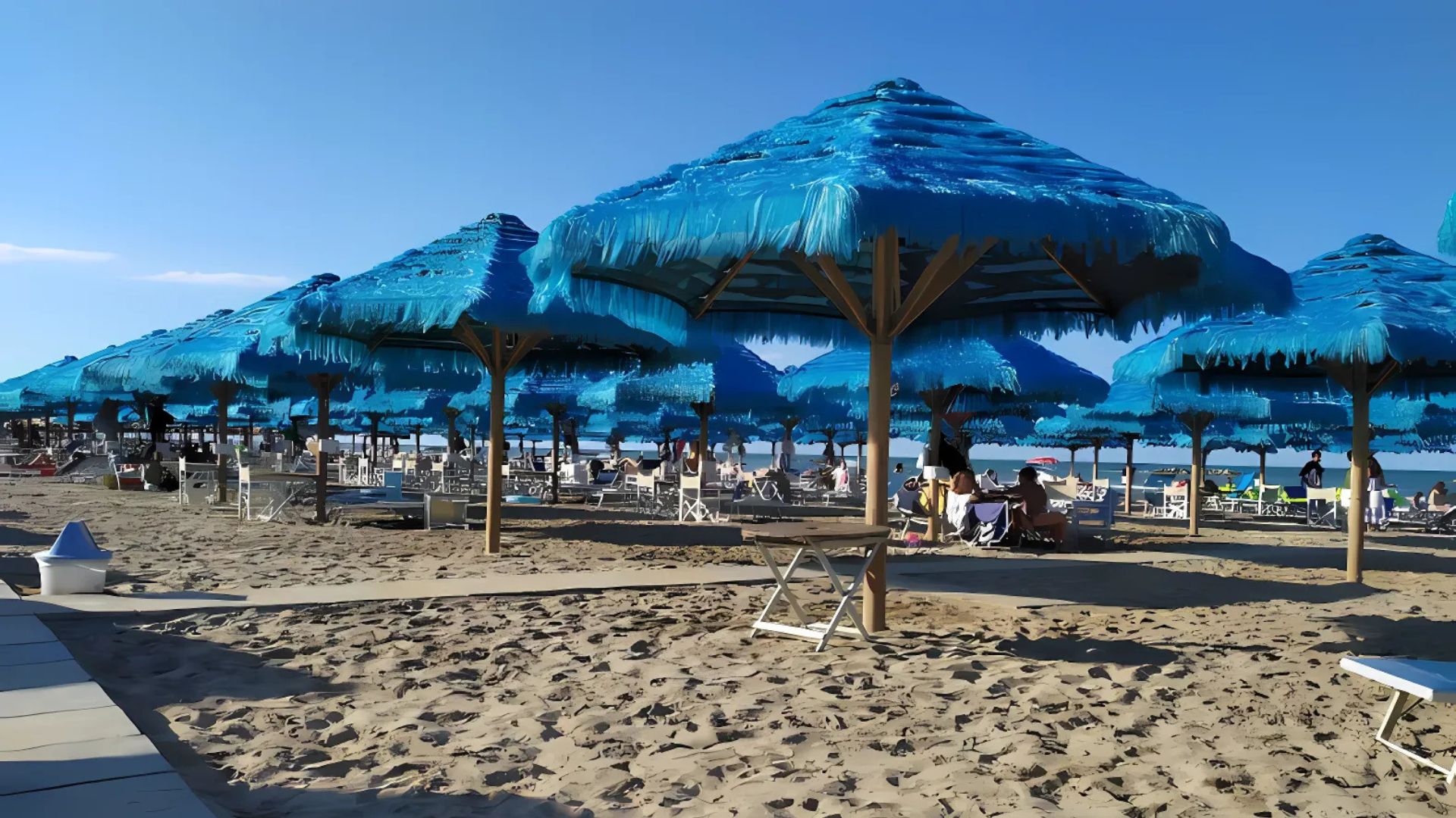 Image shows beach umbrellas, tables, and people at an "Stabilimenti" in a beach in Pescara, Italy.