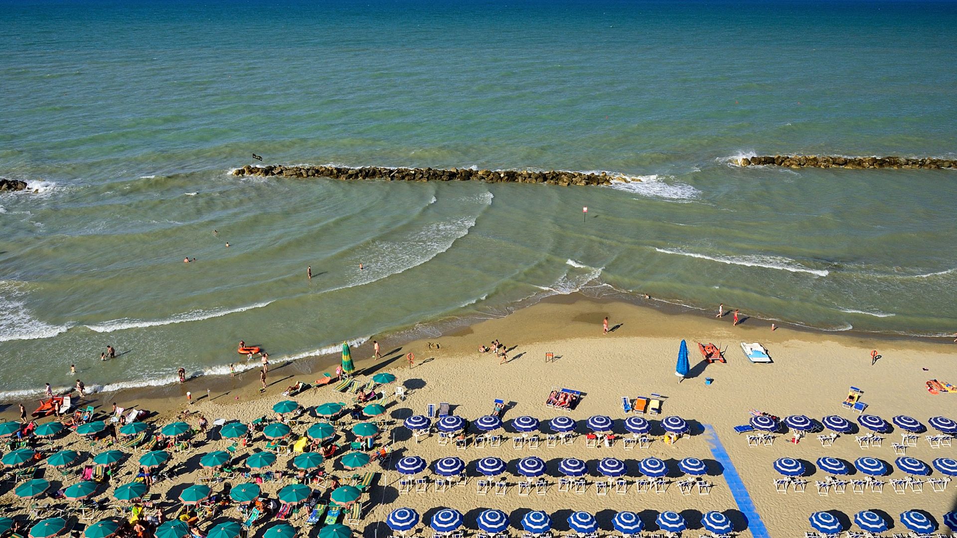 Image shows colorful umbrellas, chairs, and people on a beach in Pescara, Italy.