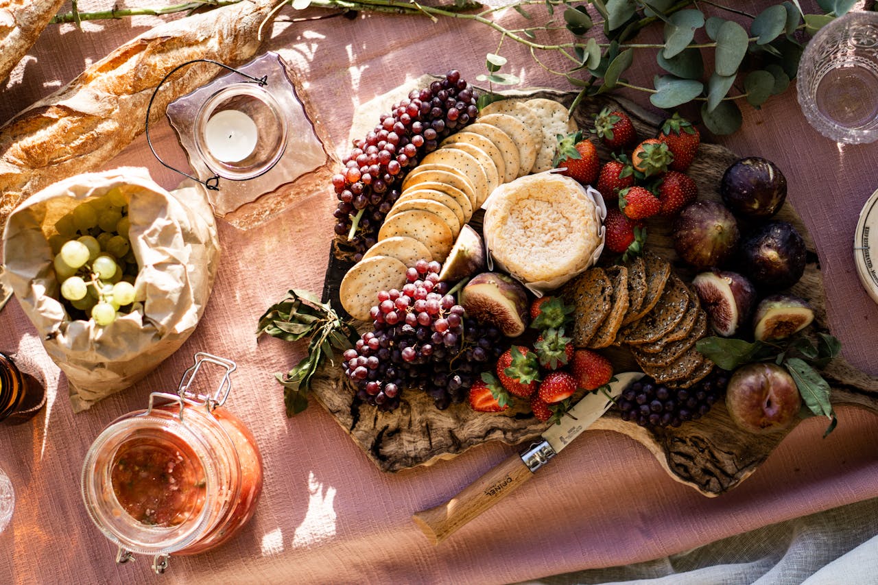 Picnic board with crackers, grapes, figs, jams, and strawberries