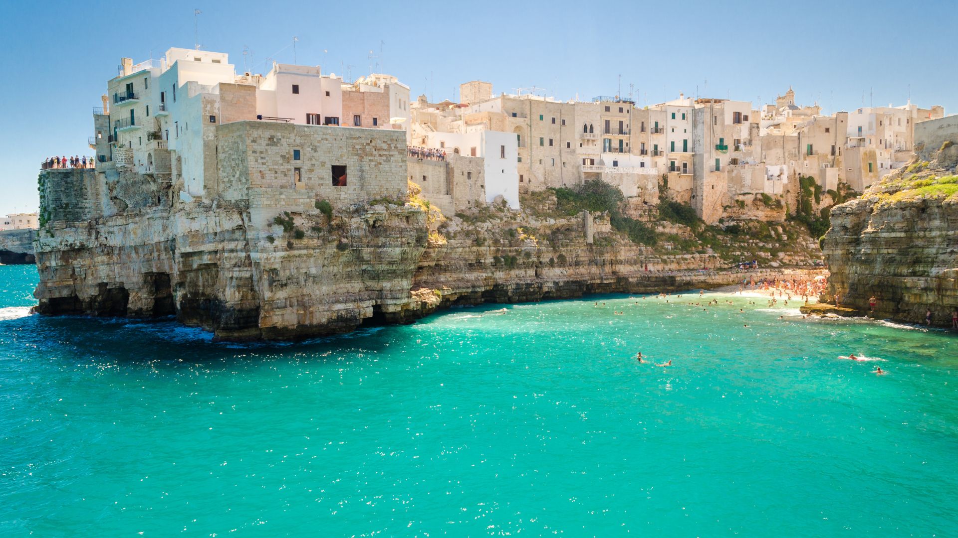Image shows turquoise water and cliff of the Polignano a Mare, Italy.  