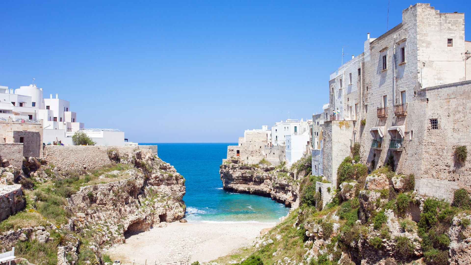 Image shows the clear turquoise water, cliff and the shore without any people on the beach of Polignano a Mare. 