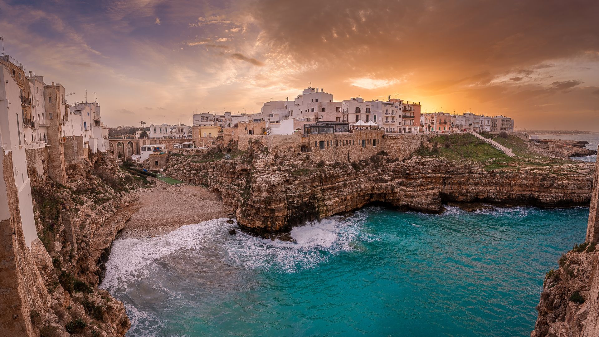 Image shows a beautiful sunset with the clear turquoise water, cliff and the shore in Polignano a Mare, Italy. 