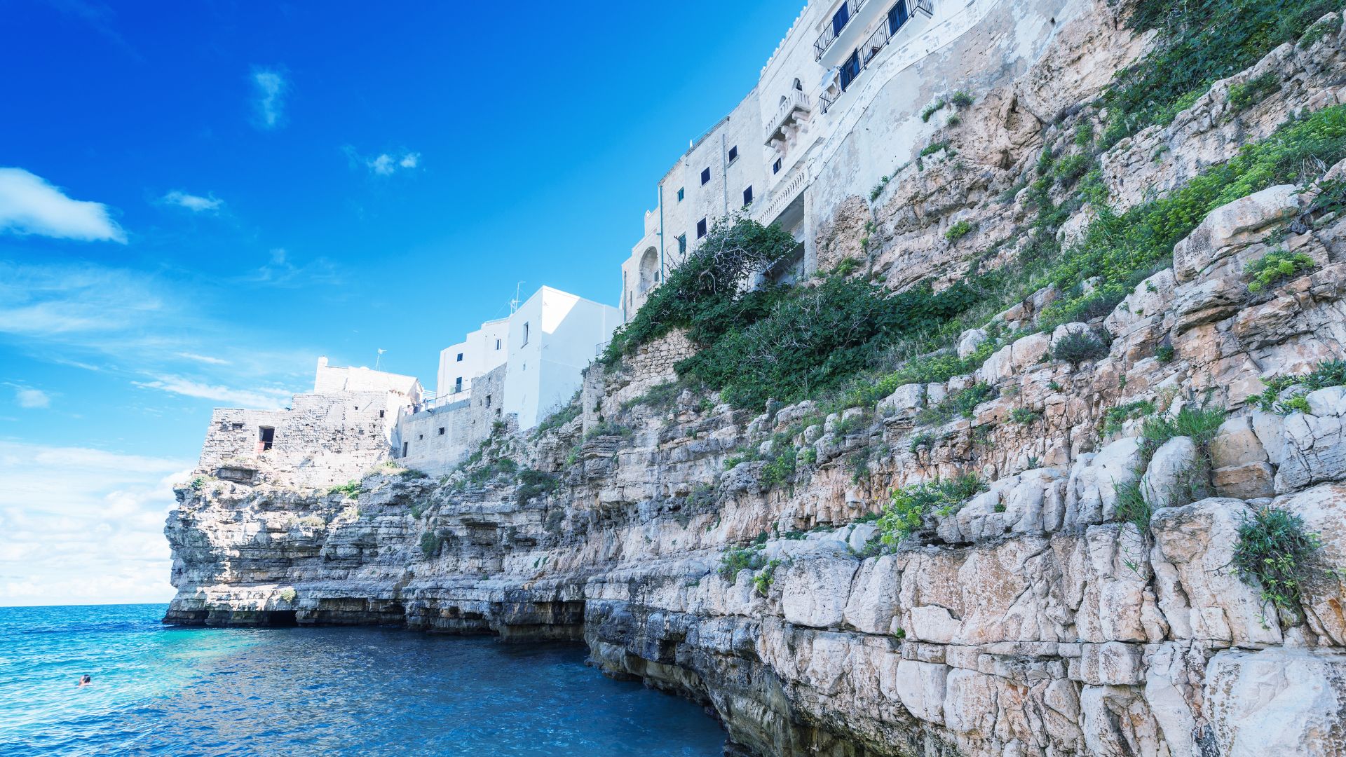 Image shows blue waters and rocky cliff of Polignano a Mare, Italy