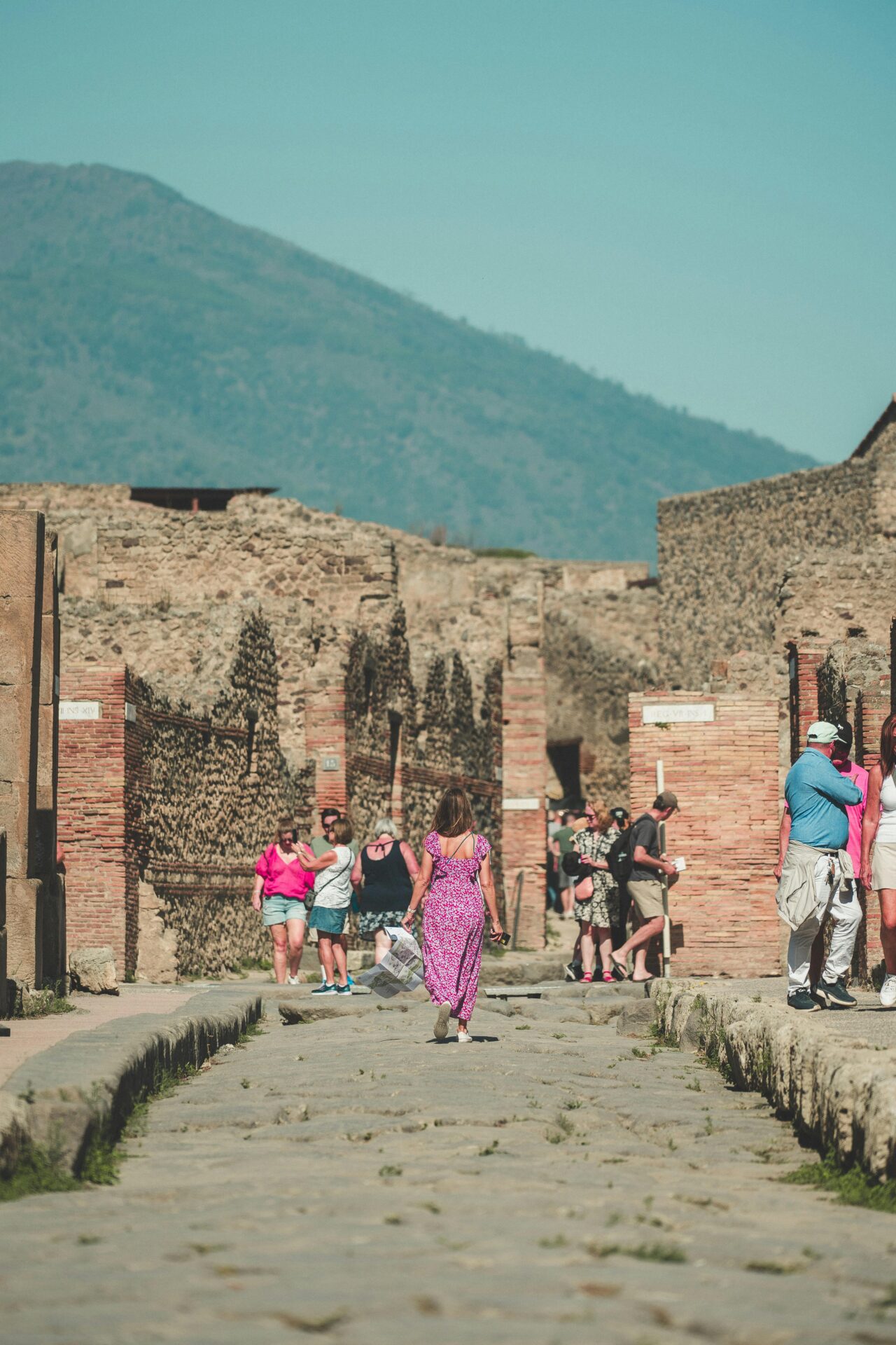 Tourist exploring the ancient ruins of Pompeii, walking along a stone-paved street lined with historic buildings and remnants of Roman architecture.