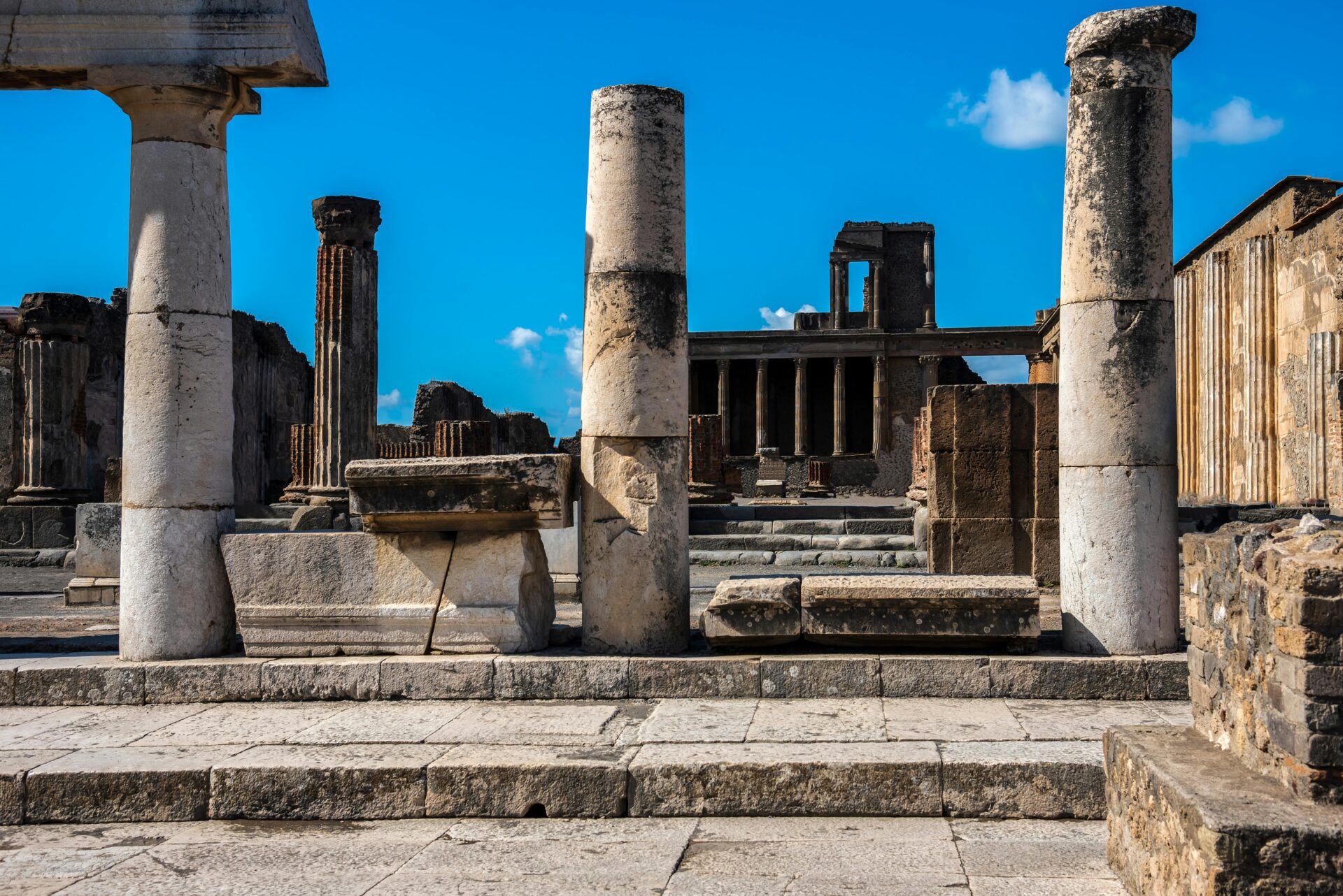 Ancient stone columns and ruins at the archaeological site of Pompeii, Italy, under a clear blue sky.