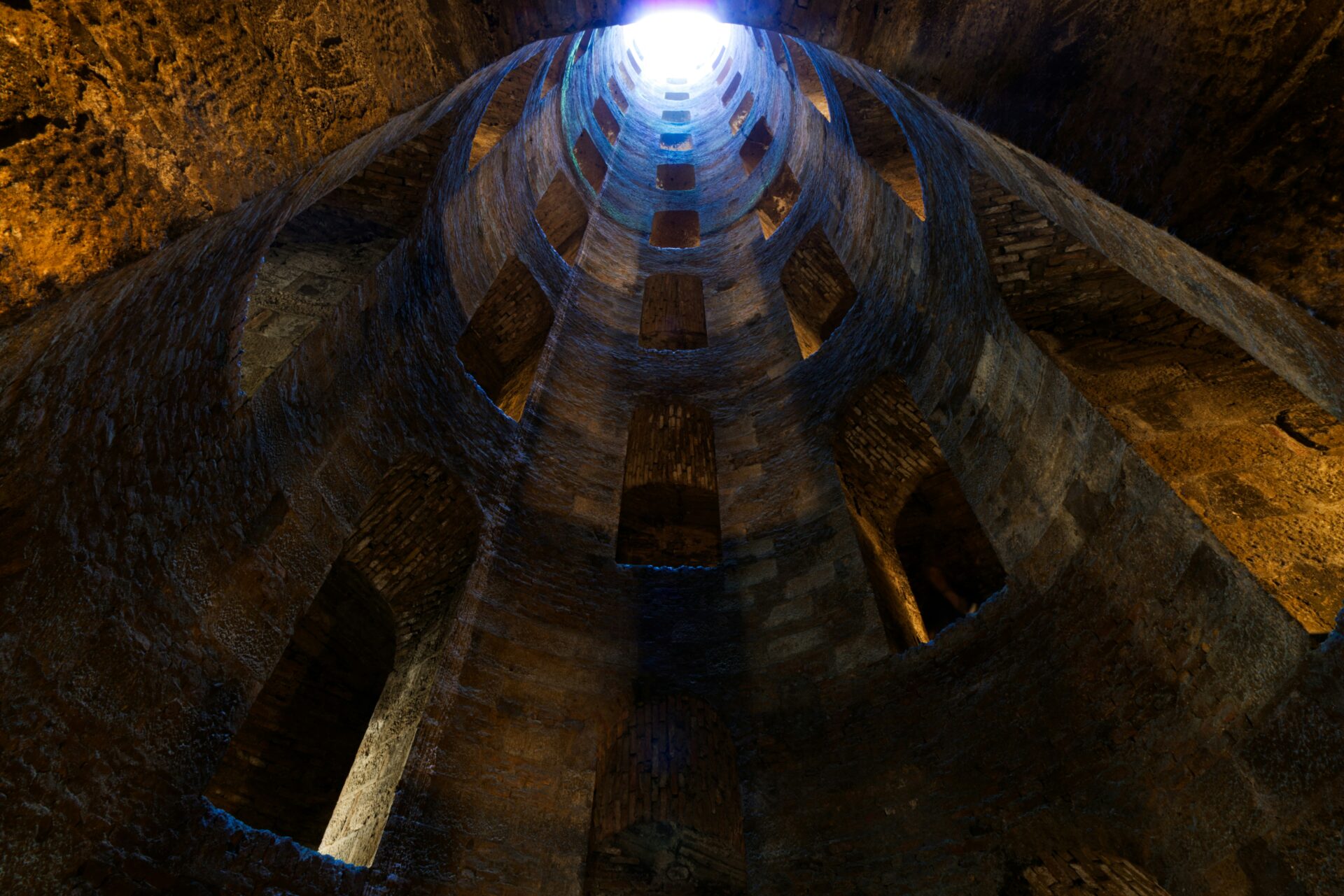 Dramatic downward view into Pozzo di San Patrizio in Orvieto, Italy, highlighting its spiraling double-helix staircases and medieval stone architecture.
