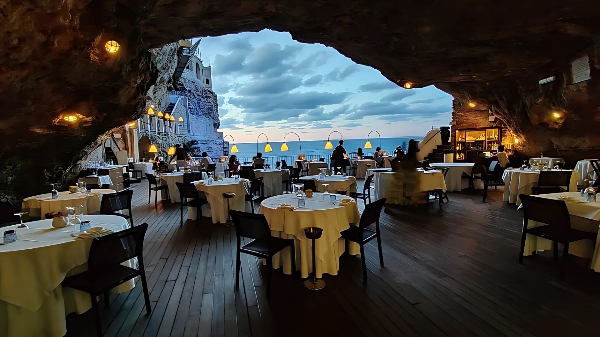 Image shows tables and chairs at the dining area of Ristorante Grotta Palazzese overlooking the Polignano a Mare
