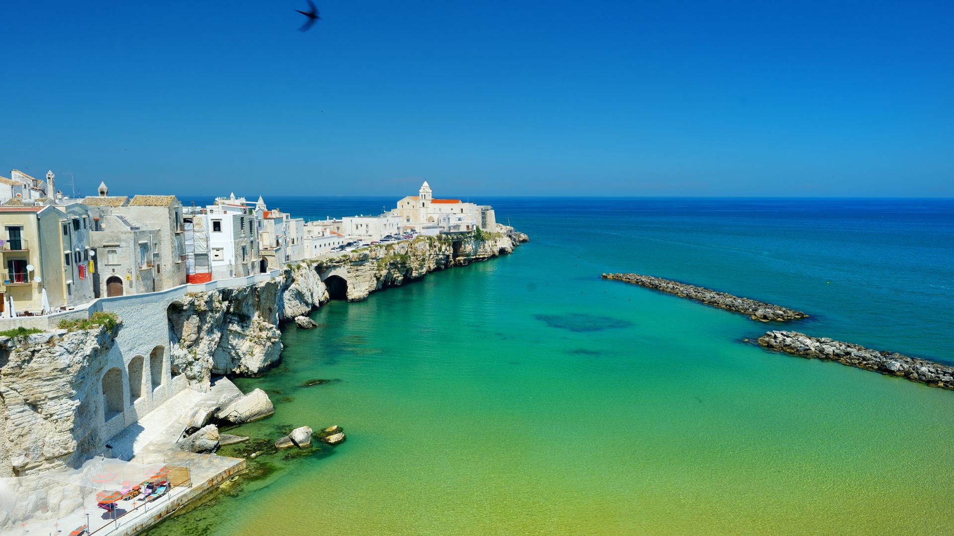 The image shows a coastal landscape featuring a natural arch formation, known as an arch or sea arch, in the Gargano National Park, located in the Apulia region of southeastern Italy.