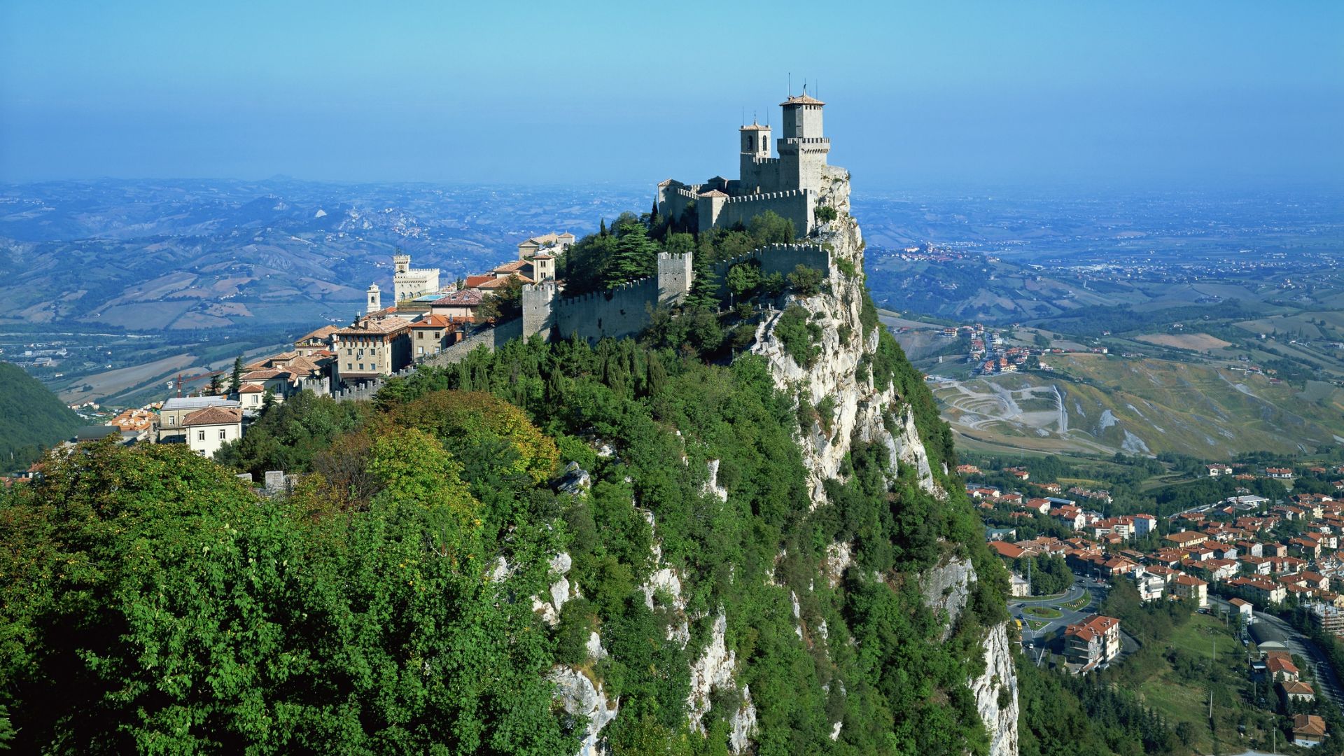 Aerial view of San Marino's Guaita Tower on Mount Titano, surrounded by lush hills and countryside.