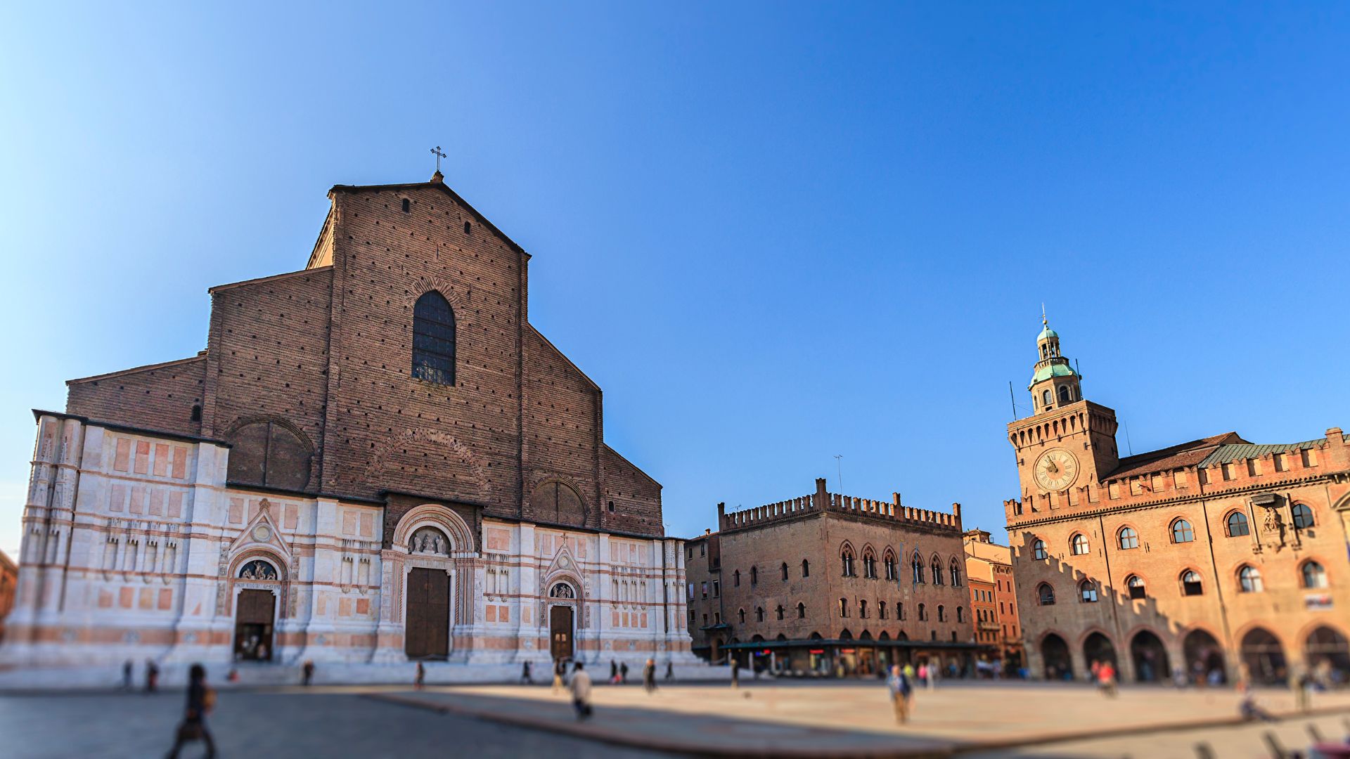 Basilica di San Petronio and Piazza Maggiore in Bologna, Italy, showcasing the architectural details of the basilica's facade and the surrounding square with other historical buildings under a clear blue sky.