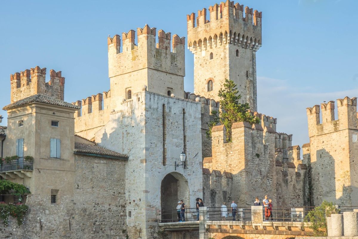 Scaliger Castle is a medieval fortress located in Sirmione, on the shores of Lake Garda in northern Italy. Built in the 13th century by the Scaliger family, who ruled Verona, the castle is a well-preserved example of medieval architecture and features imposing walls, towers, and a harbor. It is surrounded by a moat and accessible via a drawbridge, making it a picturesque and historically significant landmark. 