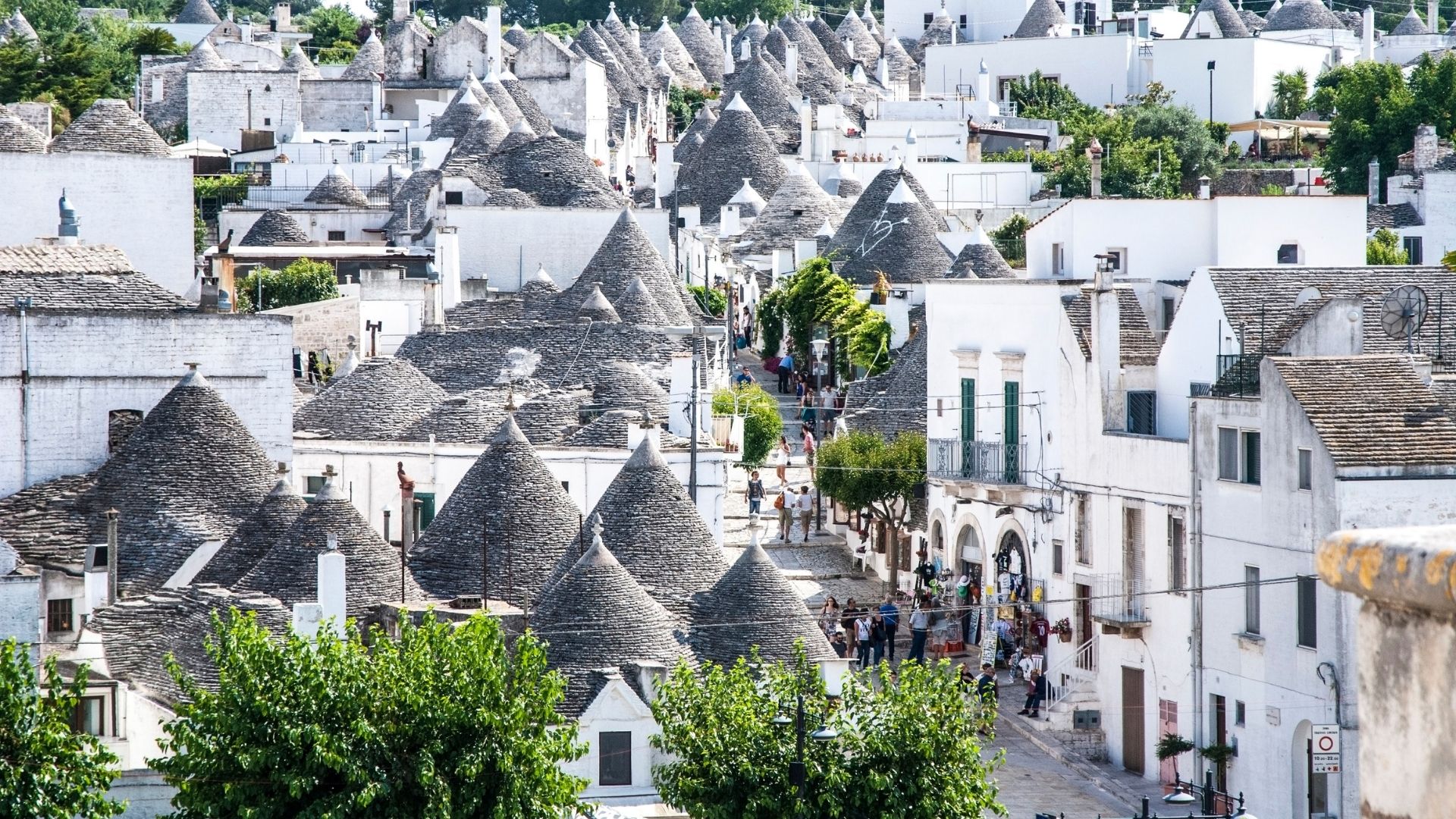 Trulli houses in Alberobello, Italy are shown in the image. Trulli are traditional dry stone huts with conical roofs, unique to the Apulia region of southern Italy. These structures are characterized by their white-washed walls and gray stone roofs, often adorned with symbolic or religious markings.
