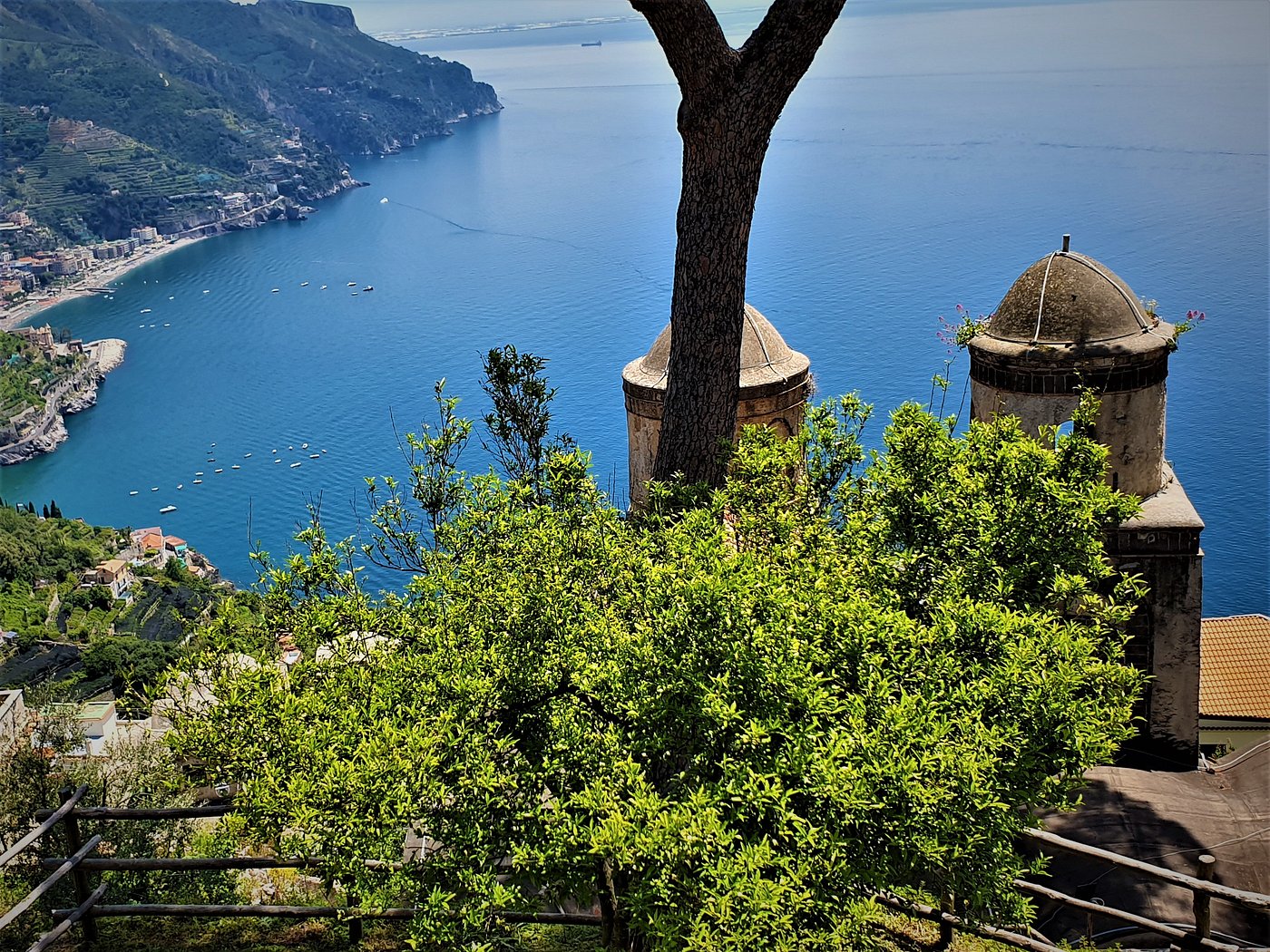 View from the terrace of Villa Rufolo in Ravello, Italy, overlooking the coastline and blue sea with historic towers and lush greenery in the foreground.