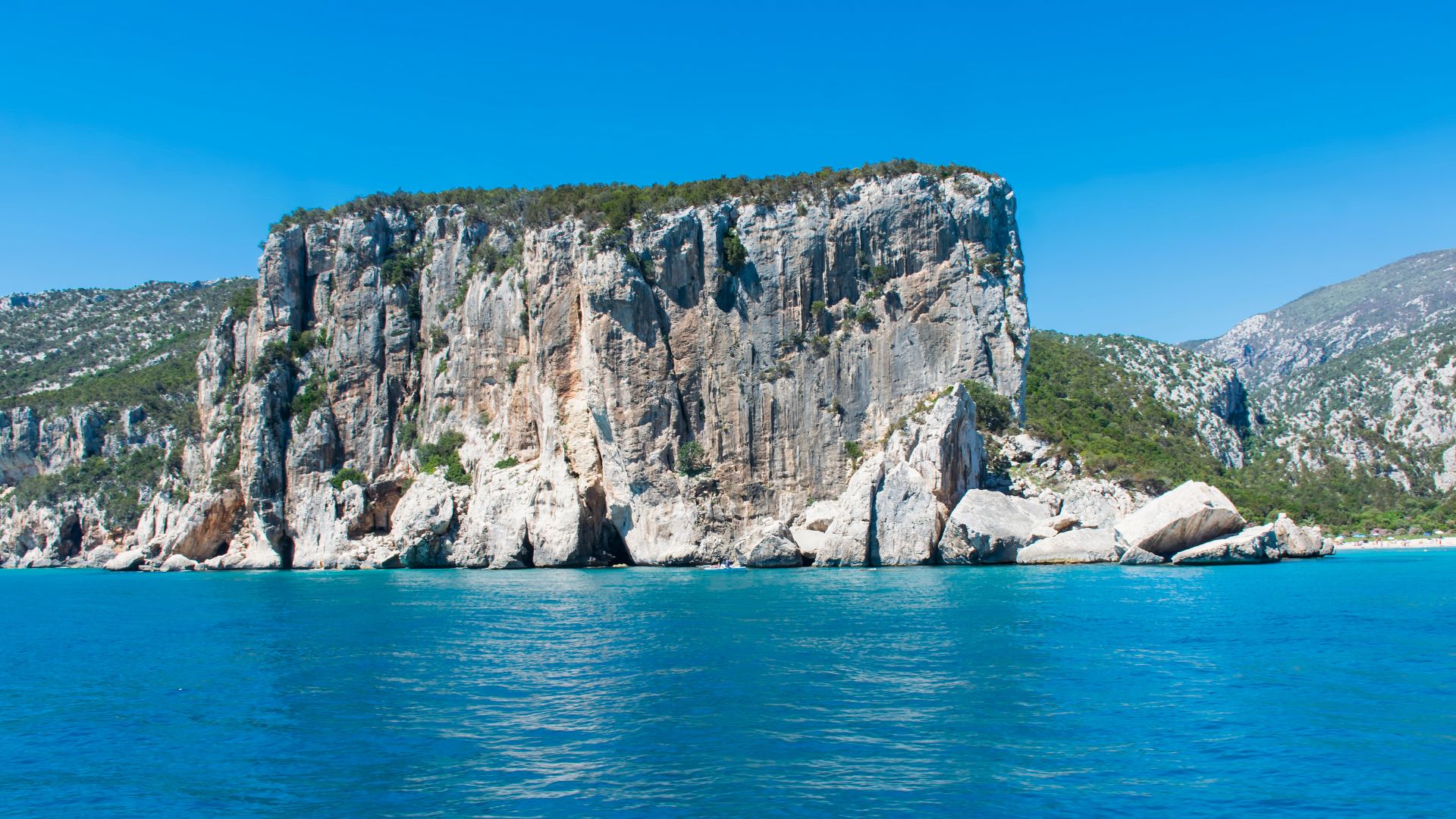 Cala Luna beach in Sardinia, featuring a crescent-shaped sandy beach, towering limestone cliffs, and the blue waters of the Gulf of Orosei.