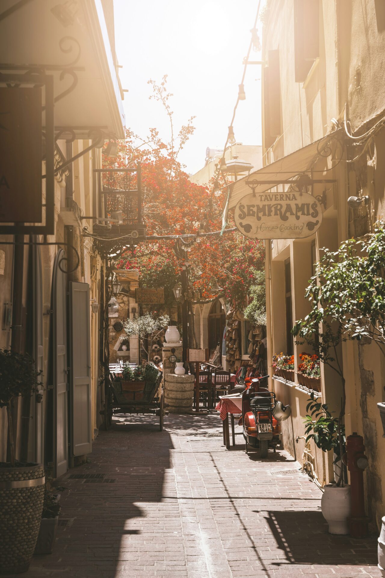 Narrow cobblestone street in Rethymno, Crete, lined with old buildings and flowering plants.