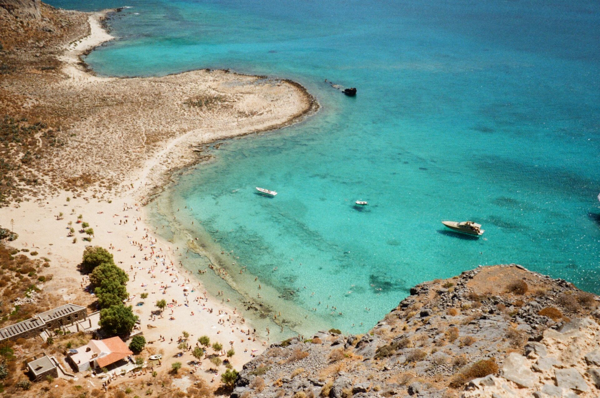 Aerial view of Balos Lagoon in Crete, featuring vivid turquoise waters, white sandy shores, and shallow tidal pools blending into the surrounding rocky landscape