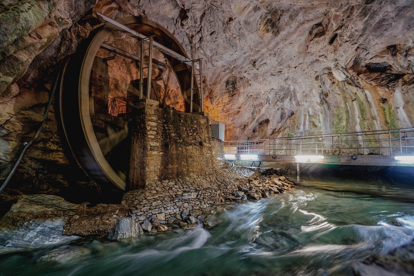 Interior view of Aggitis Cave with stalactites and a flowing river.