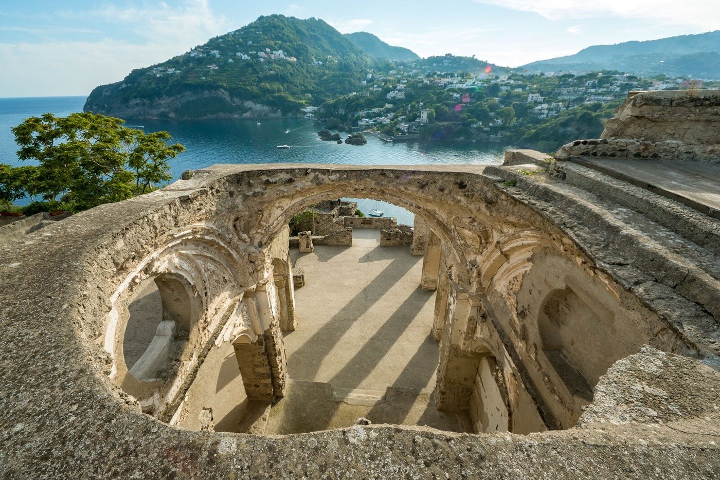 Ruins of the Aragonese Castle in Ischia, Italy, overlooking the sea and green hills in the background.