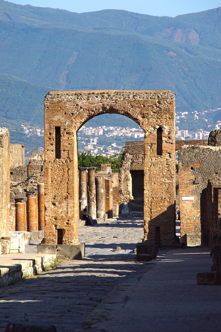 Ancient stone archway and ruins at the Archaeological Park of Pompeii, with a mountain backdrop.