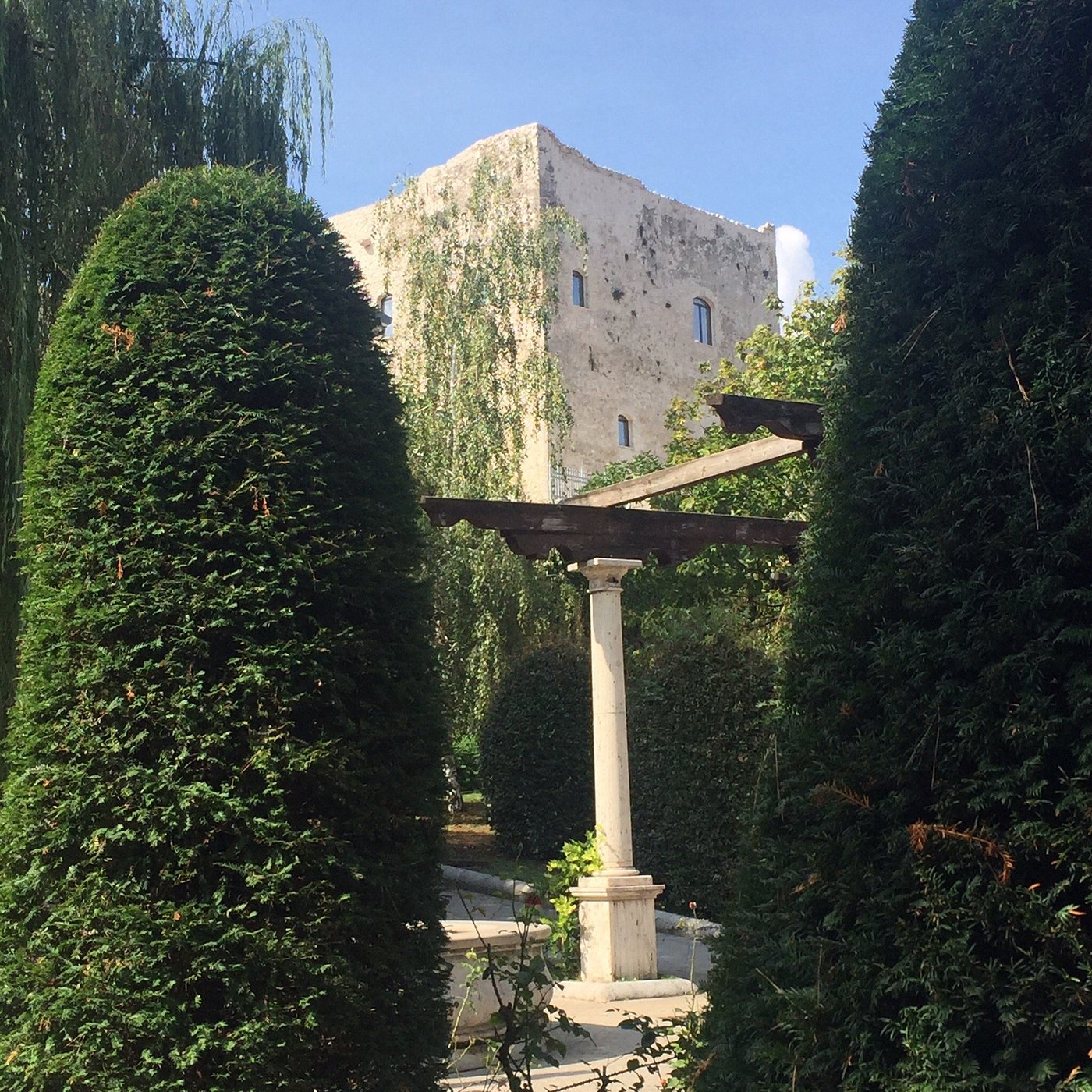 Garden view with manicured hedges and an old stone building in Bagnoli Irpino, Italy.