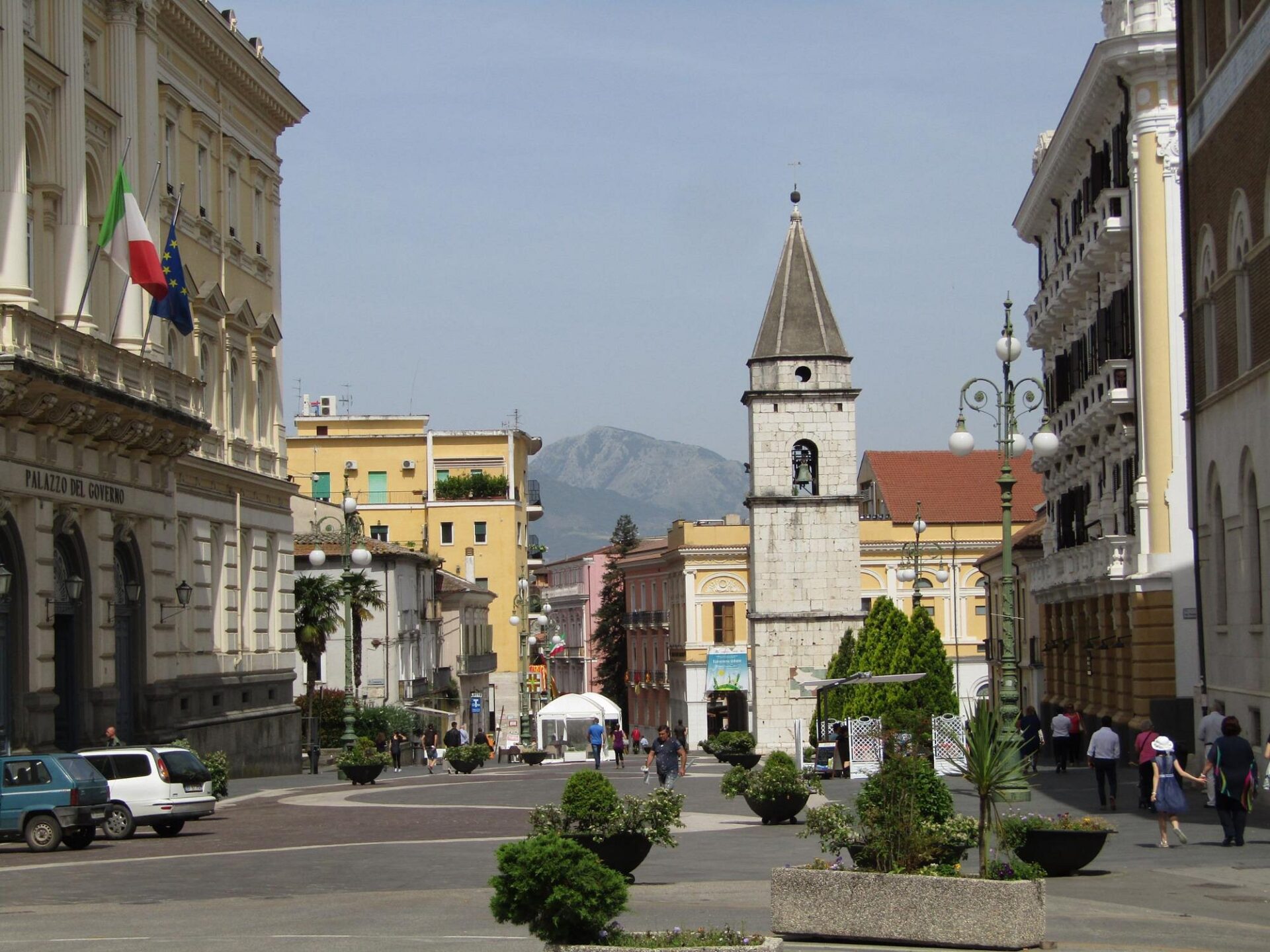 Charming town square with historic buildings, a bell tower, and people walking in Benevento, Italy.