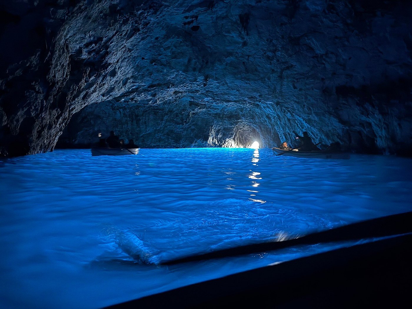 Boats floating inside the glowing blue waters of the Blue Grotto sea cave in Capri, Italy.