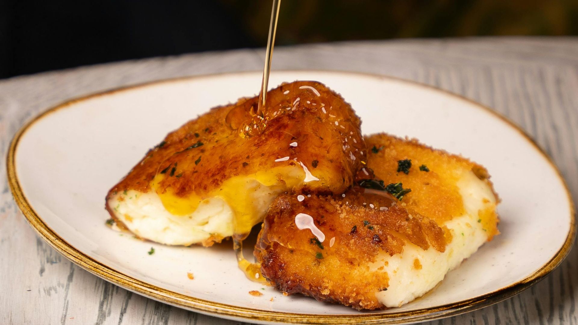 Two pieces of golden-brown bougatsa with cheese filling are drizzled with honey on a white plate.