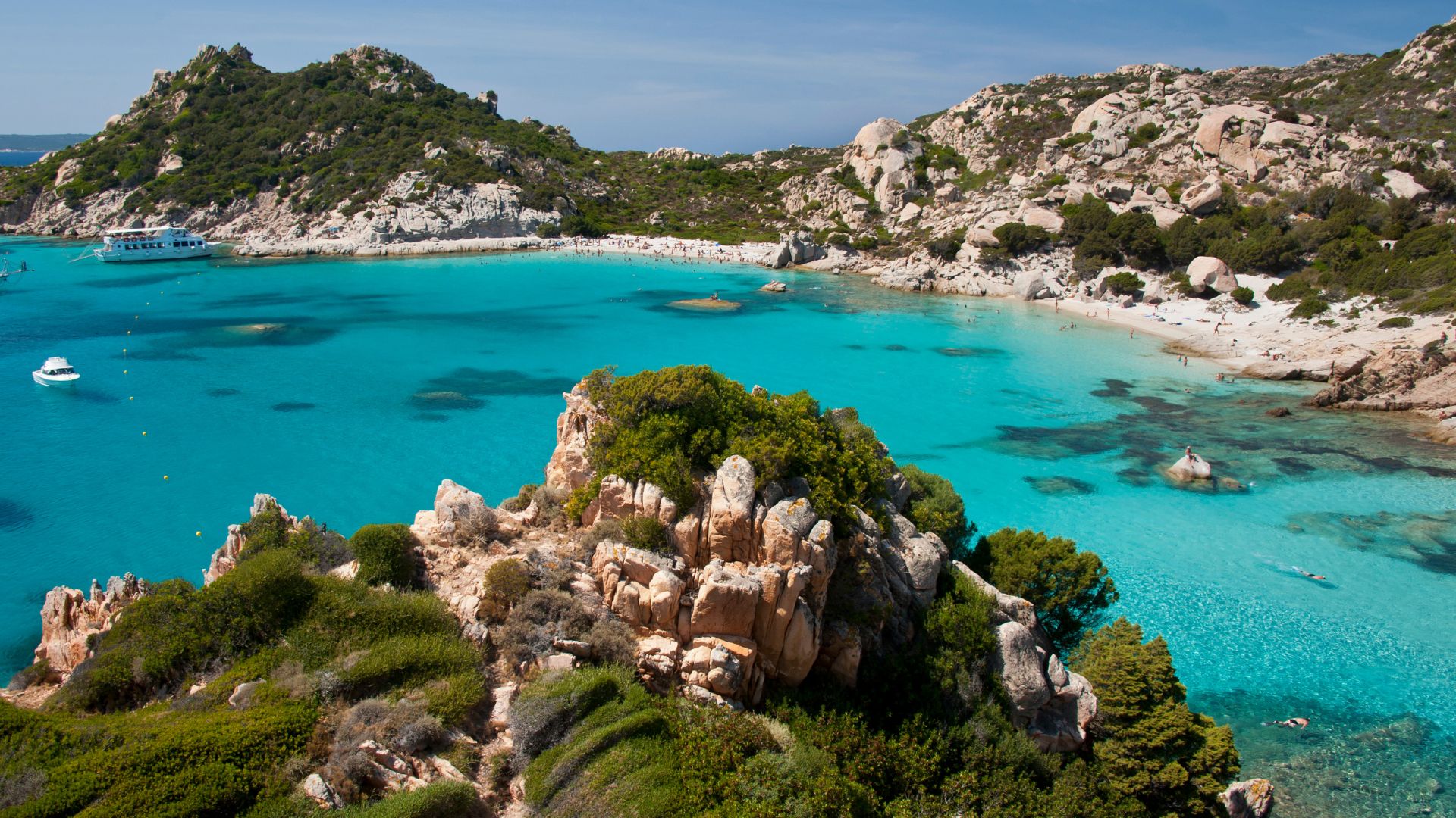 Aerial view of rocky cliffs, turquoise waters, greenery, and white sand beaches of Cala Corsara, Spargi, Sardinia, Italy. 