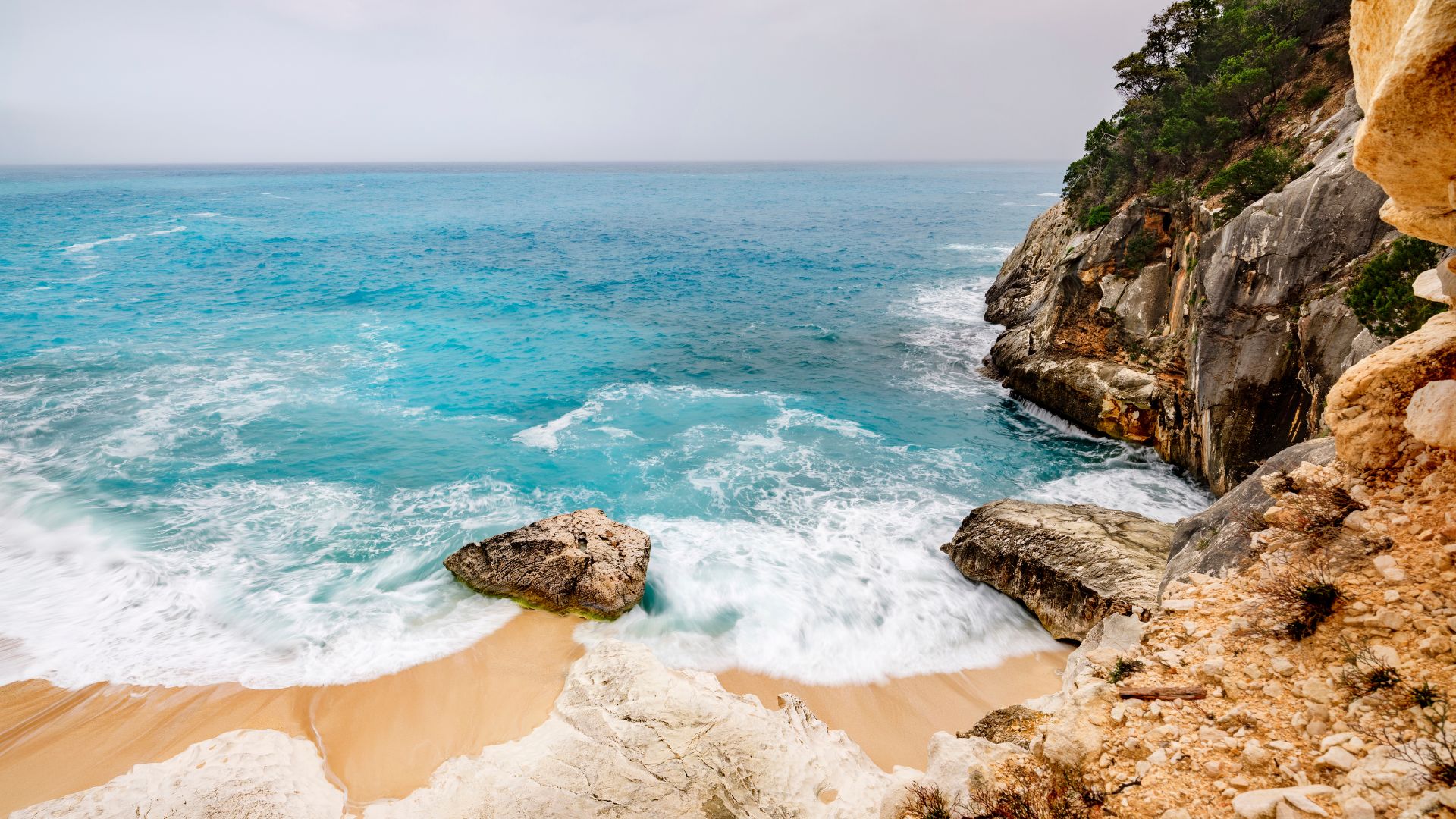 Scenic view of turquoise waters, rocky shores, and whte sand beach of Cala Goloritzé in Sardinia, Italy