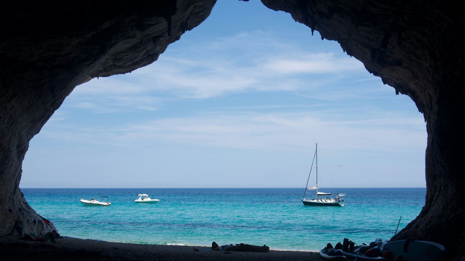 View from inside a cave looking out at Cala Luna beach in Sardinia, with boats on the water and rocky cliffs surrounding the bay.