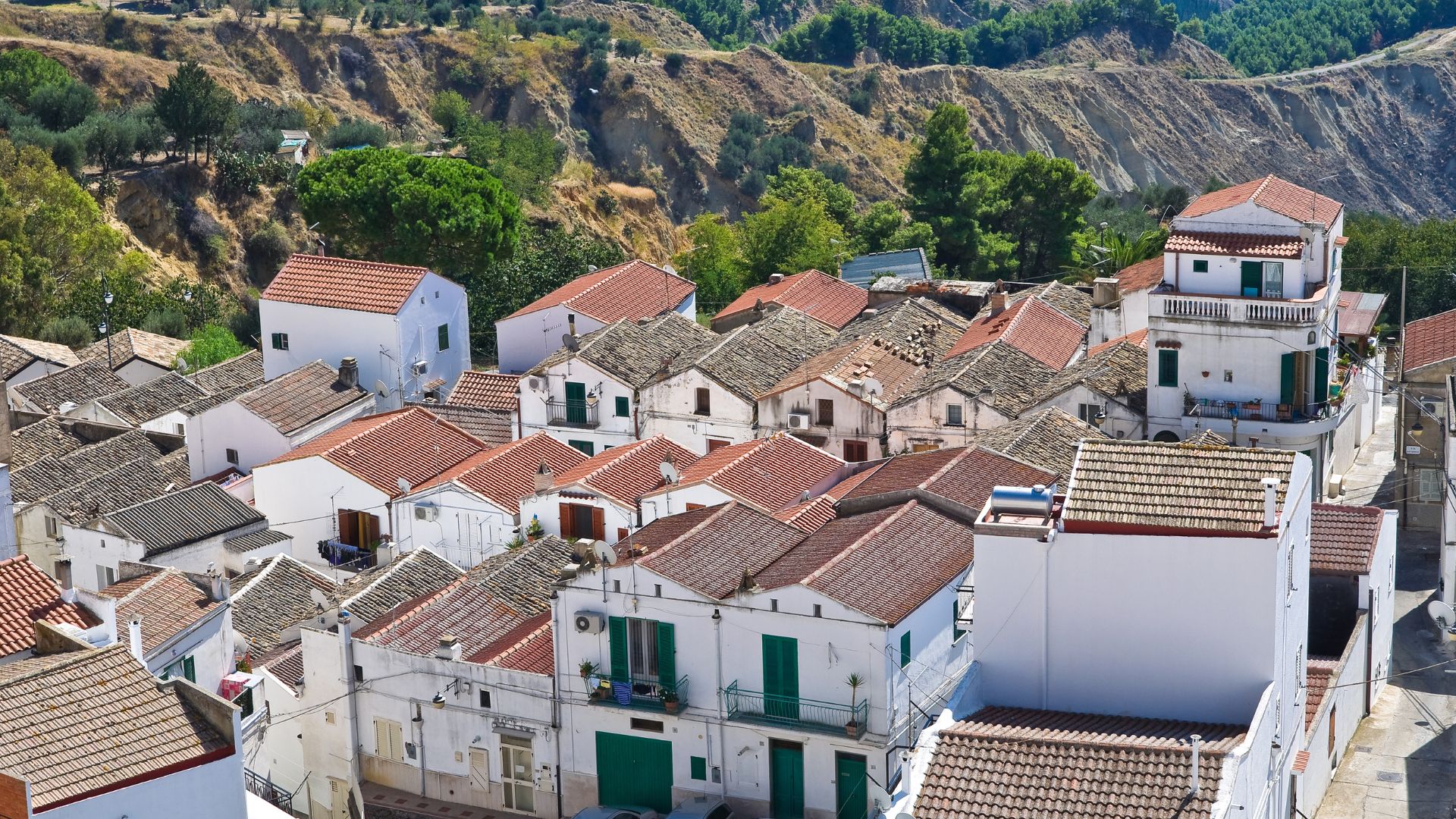 Image shows white houses, red roof and landscape of Pisticci, Italy.