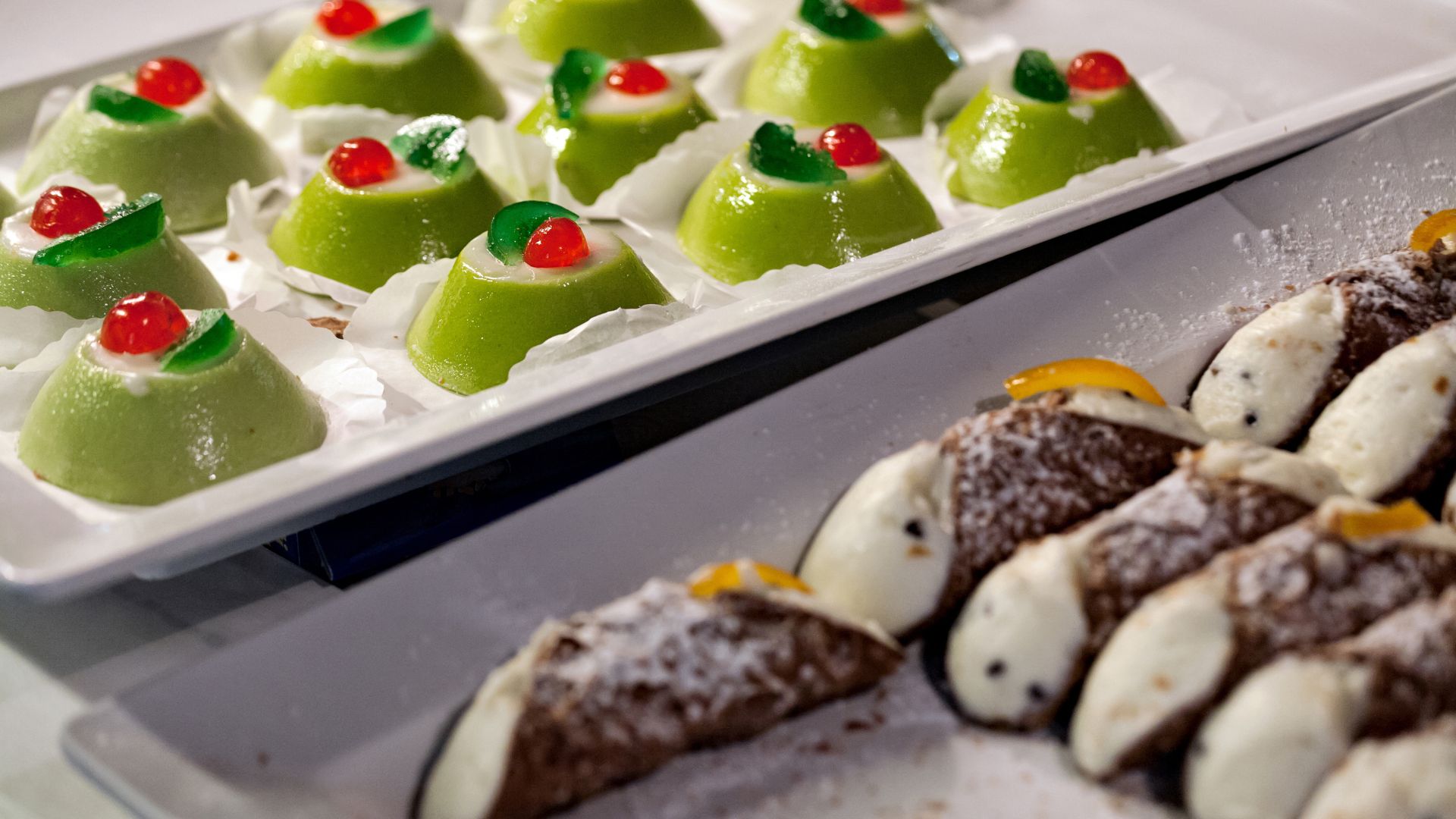 Two trays of Italian pastries, one with several cannoli and the other with small Sicilian cassata cakes.