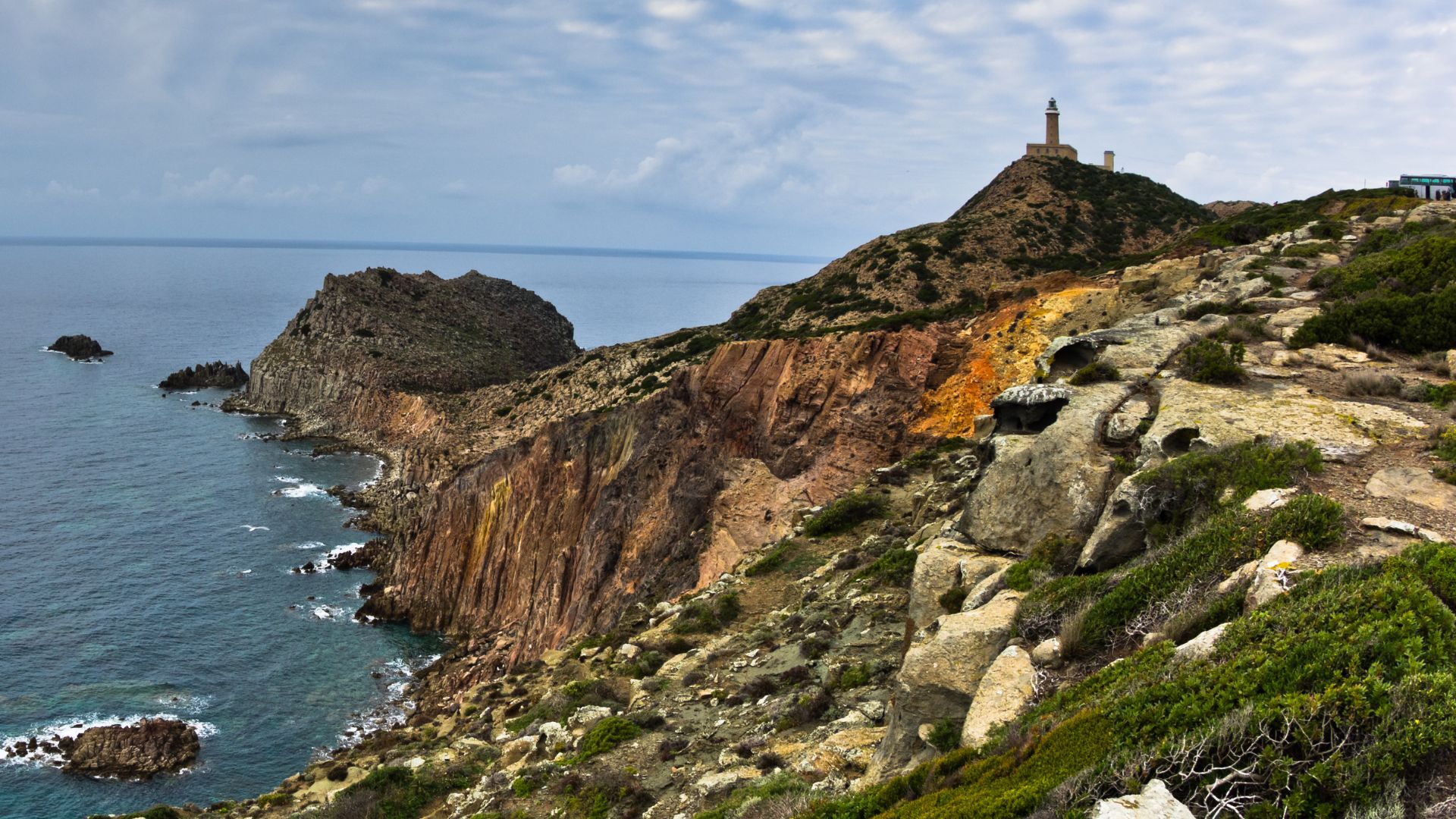 Scenic view of blue sky and waters, and lighthouse perched on rocky cliffs at Capo Sandalo in Carloforte, Sardinia, Italy