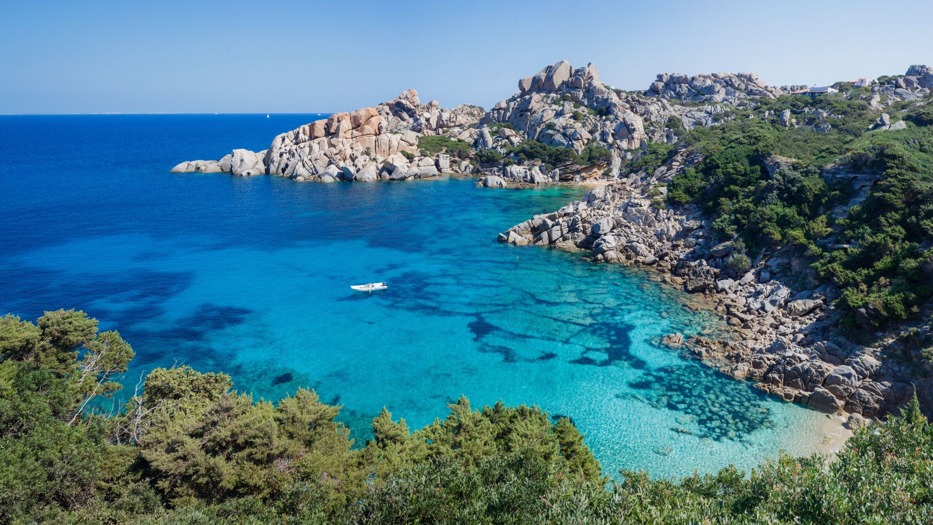 A scenic view of Capo Testa in Sardinia, Italy, featuring the rocky coastline, clear turquoise waters, and lush green vegetation.