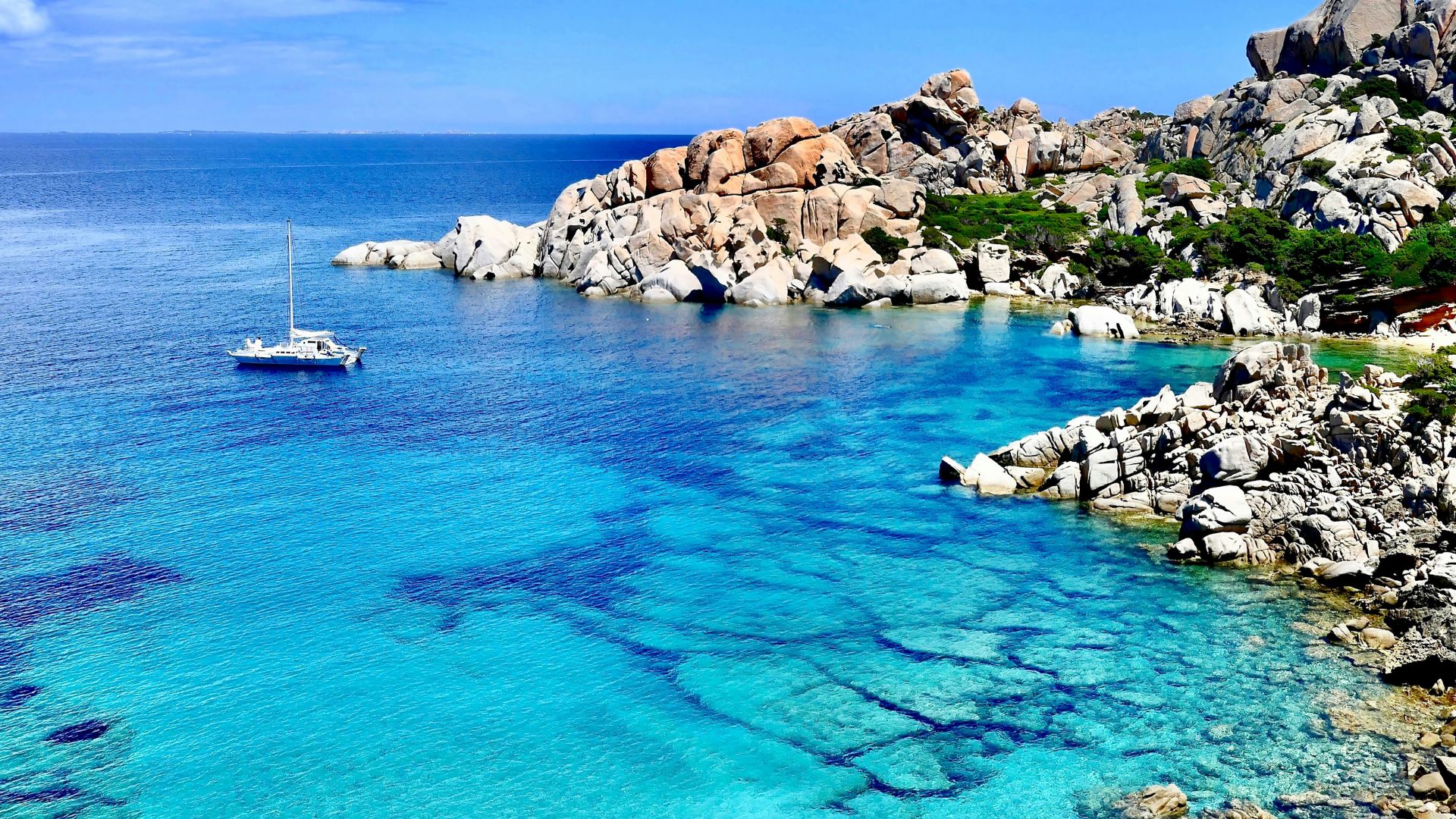 Scenic view of Capo Testa in Santa Teresa Gallura, Sardinia, Italy characterized by pristine turquoise water, rocky cliffs, and a sailing boat. 