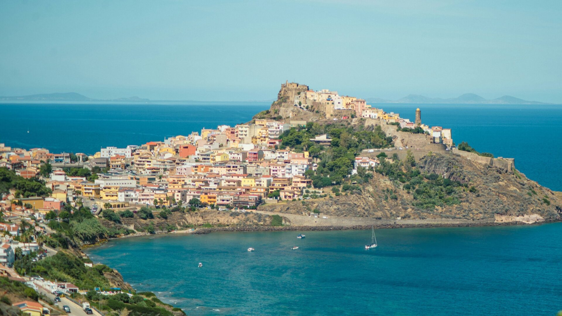 A panoramic view of the town of Castelsardo, Sardinia, featuring its hilltop castle and colorful houses overlooking the sea.
