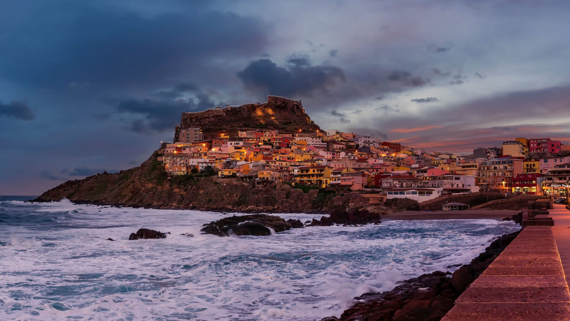 A scenic view of Castelsardo, Sardinia, featuring colorful buildings cascading down a hillside towards the sea.