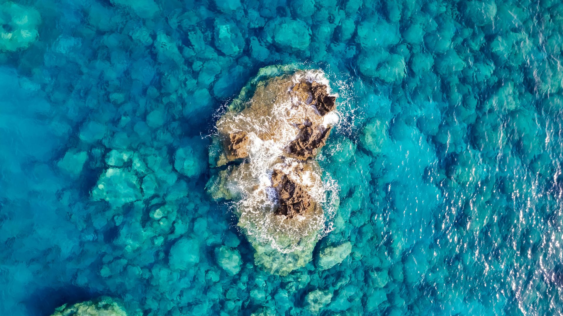 Aerial view of a rocky islet in turquoise waters.