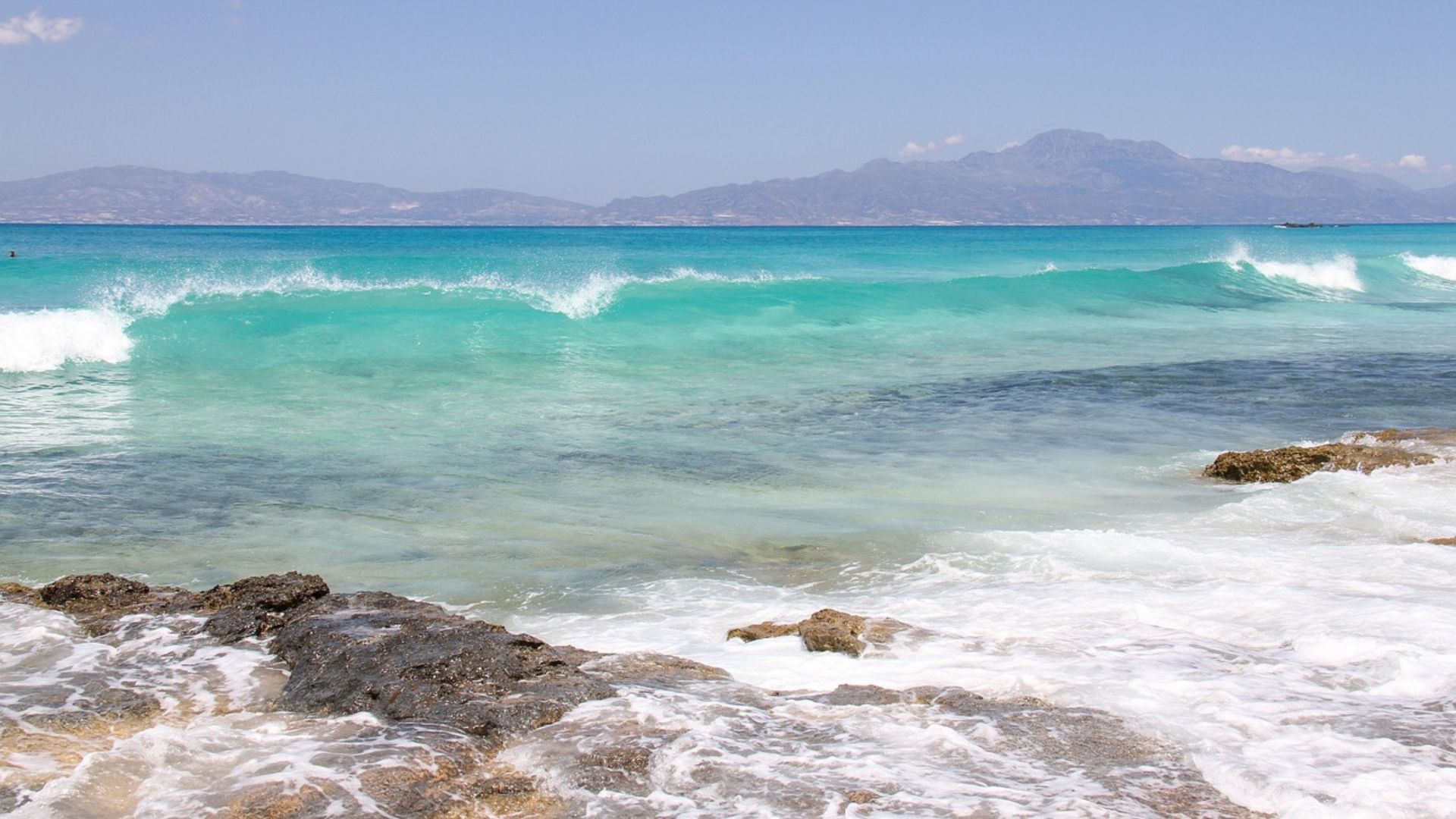 Turquoise waters and golden sands of Chrissi Island, with mountains in the distance.
