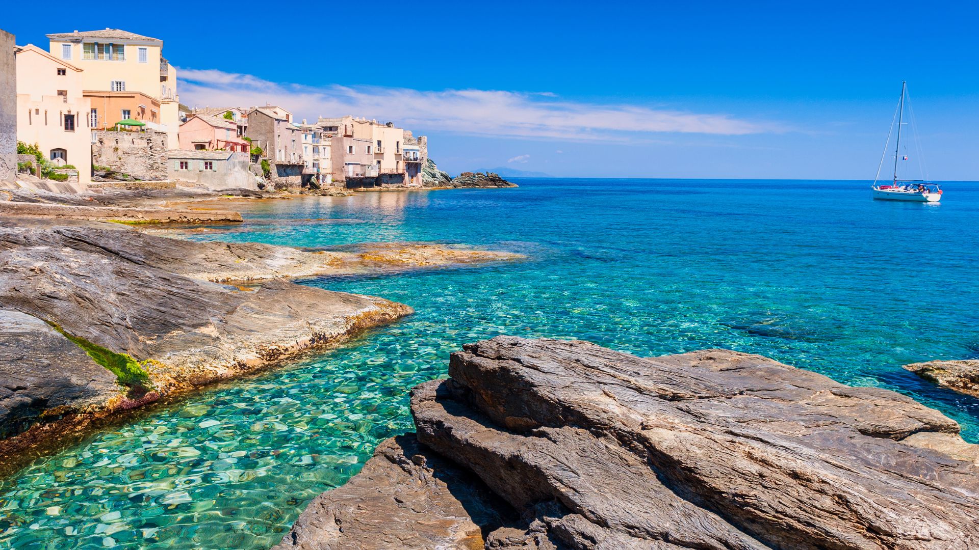Coastal village of Erbalunga, Corsica, with rocky shoreline and clear blue water.