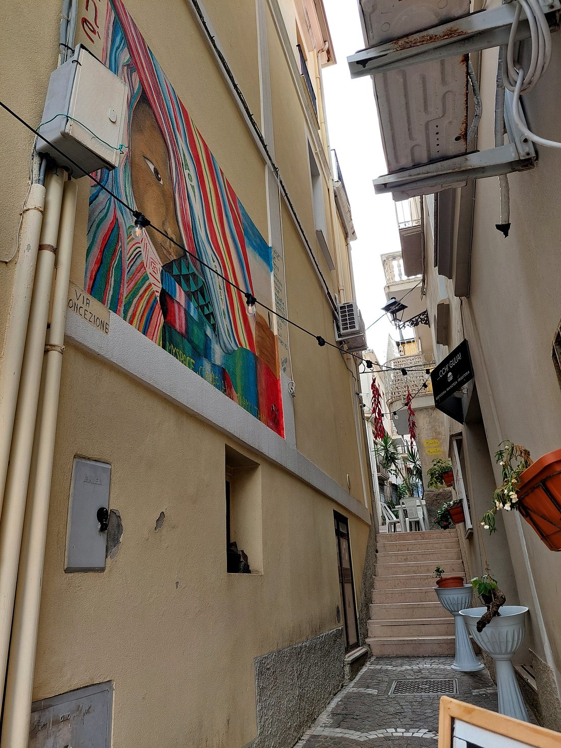Narrow cobblestone street in Diamante, Italy, flanked by old stone houses with colorful murals
