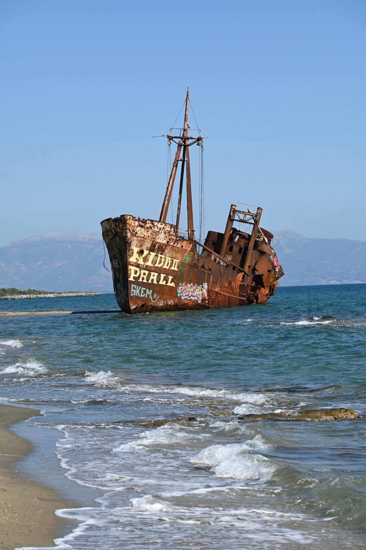A large, weathered shipwreck stranded on a beach in Gythio, Greece