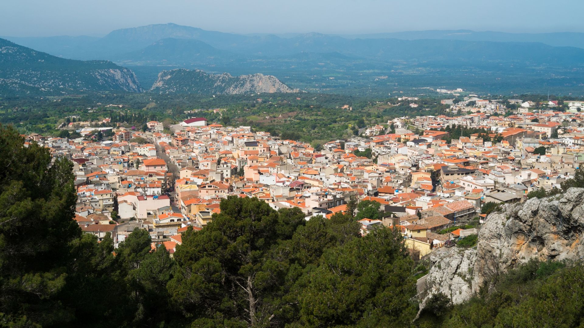 A panoramic view of Dorgali, a town in Sardinia, Italy, nestled among mountains and greenery