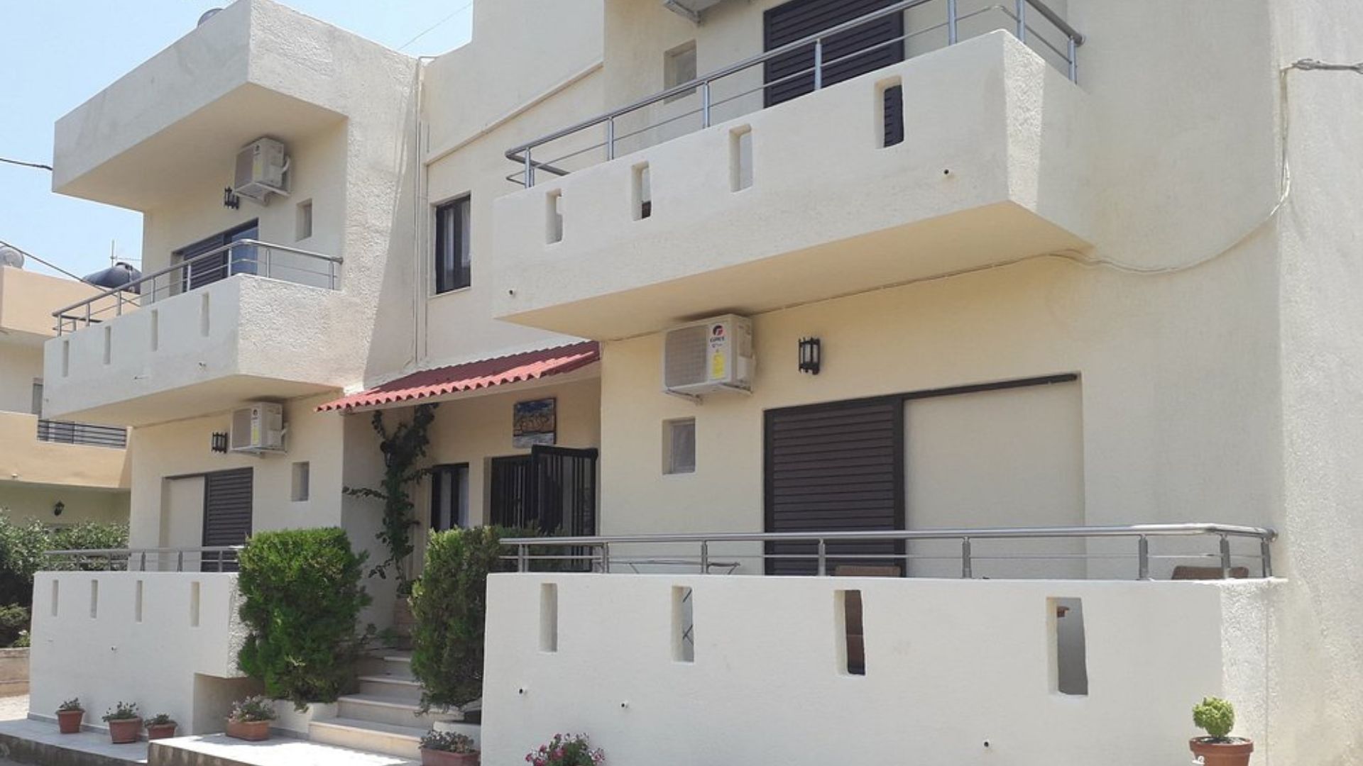 Exterior view of Elounda George Studios in Crete, featuring white buildings with balconies and greenery.