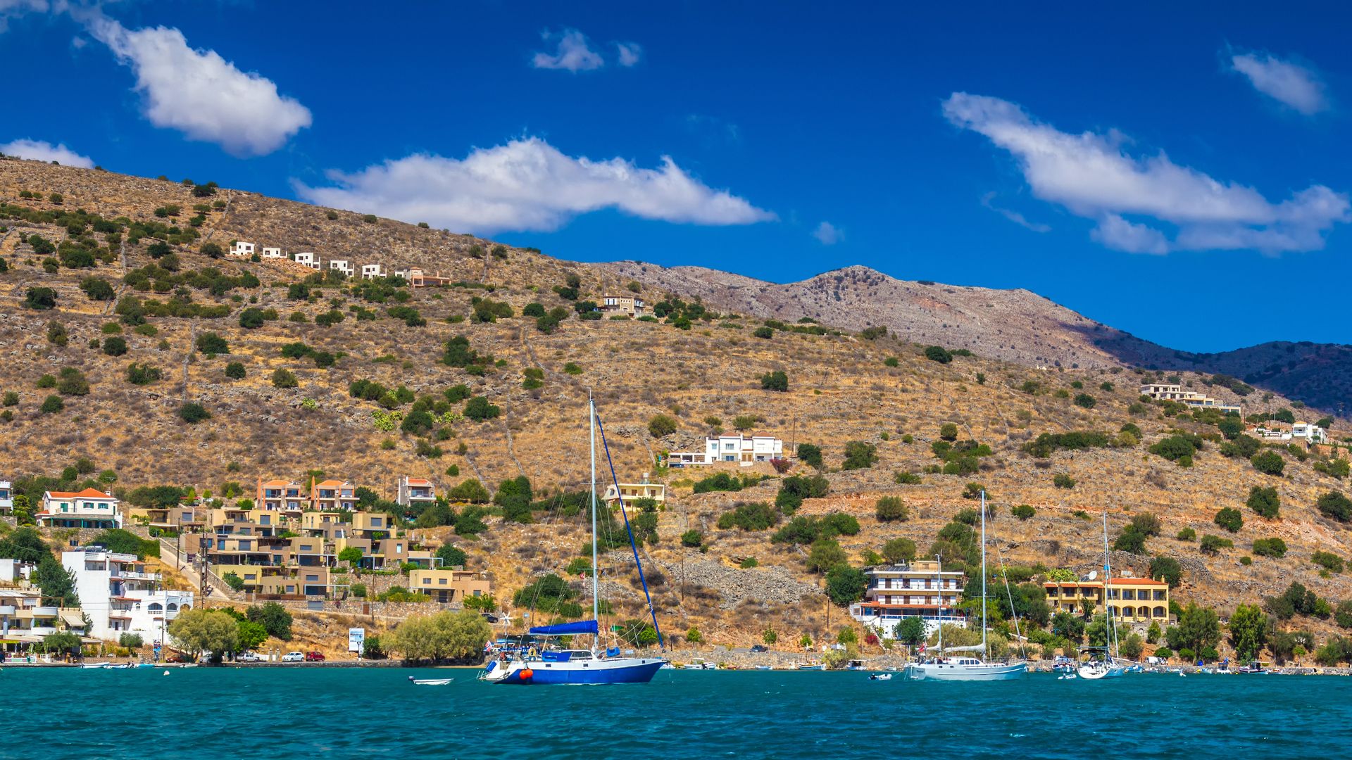 Coastal view of Elounda, Crete, featuring the Mirabello Bay with boats and hillside residences.