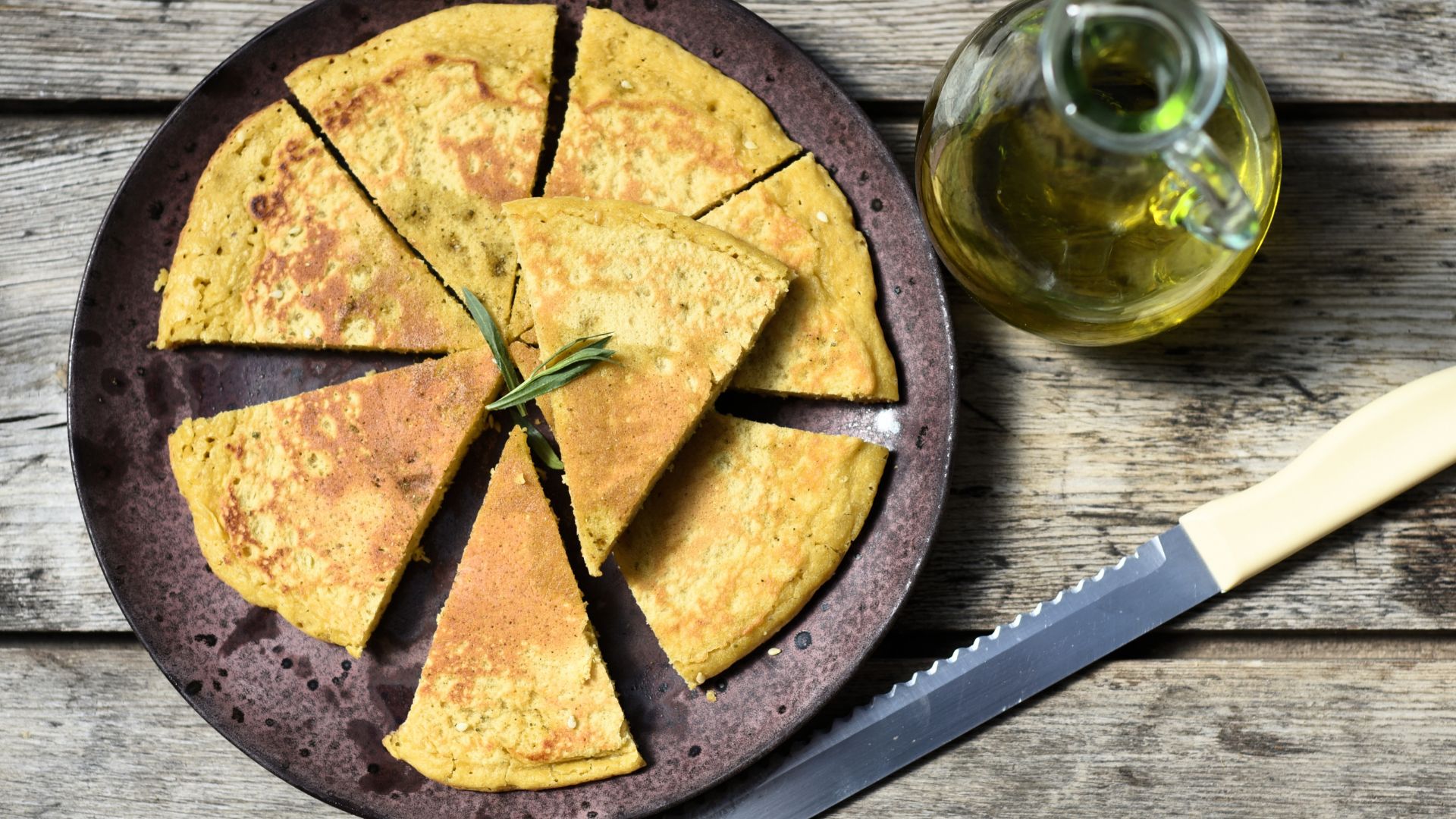 A sliced farinata on a plate, with a bottle of olive oil and a knife on the side.