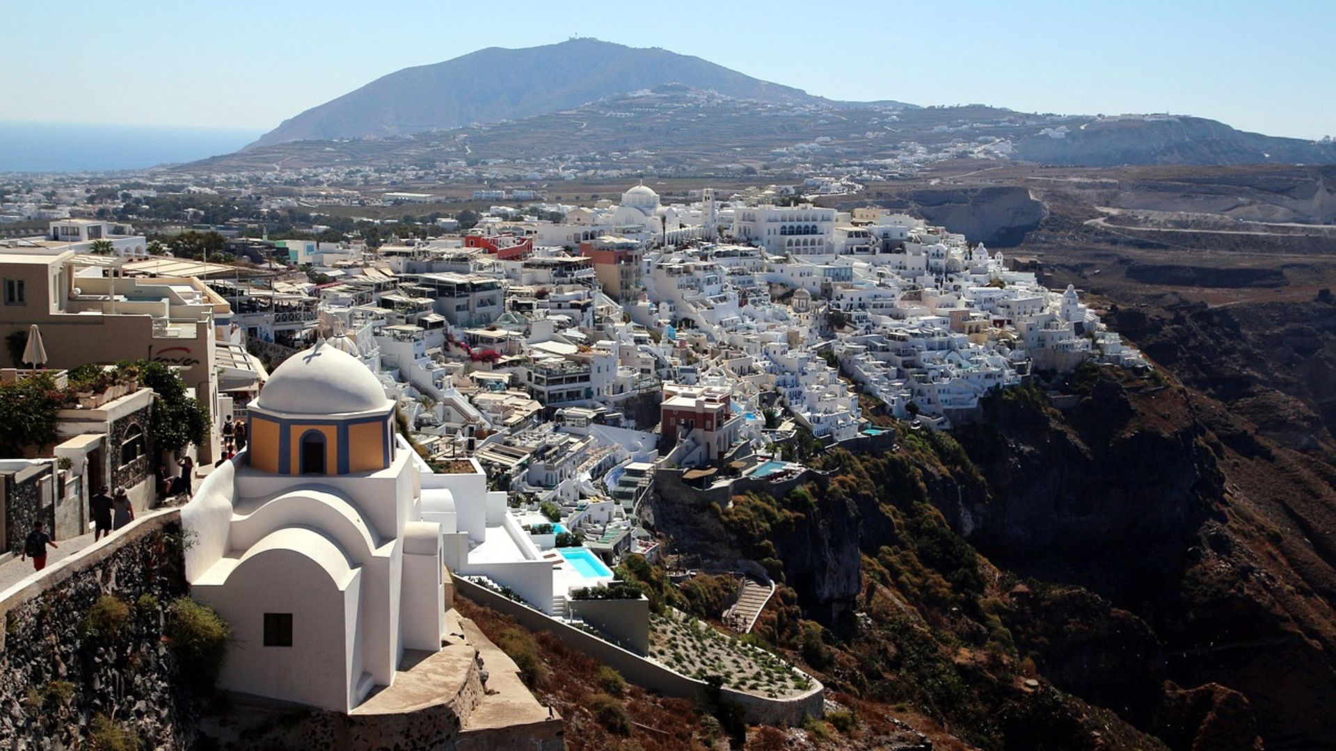 An aerial view of Fira, Santorini, featuring white buildings on a cliffside overlooking the Aegean Sea.