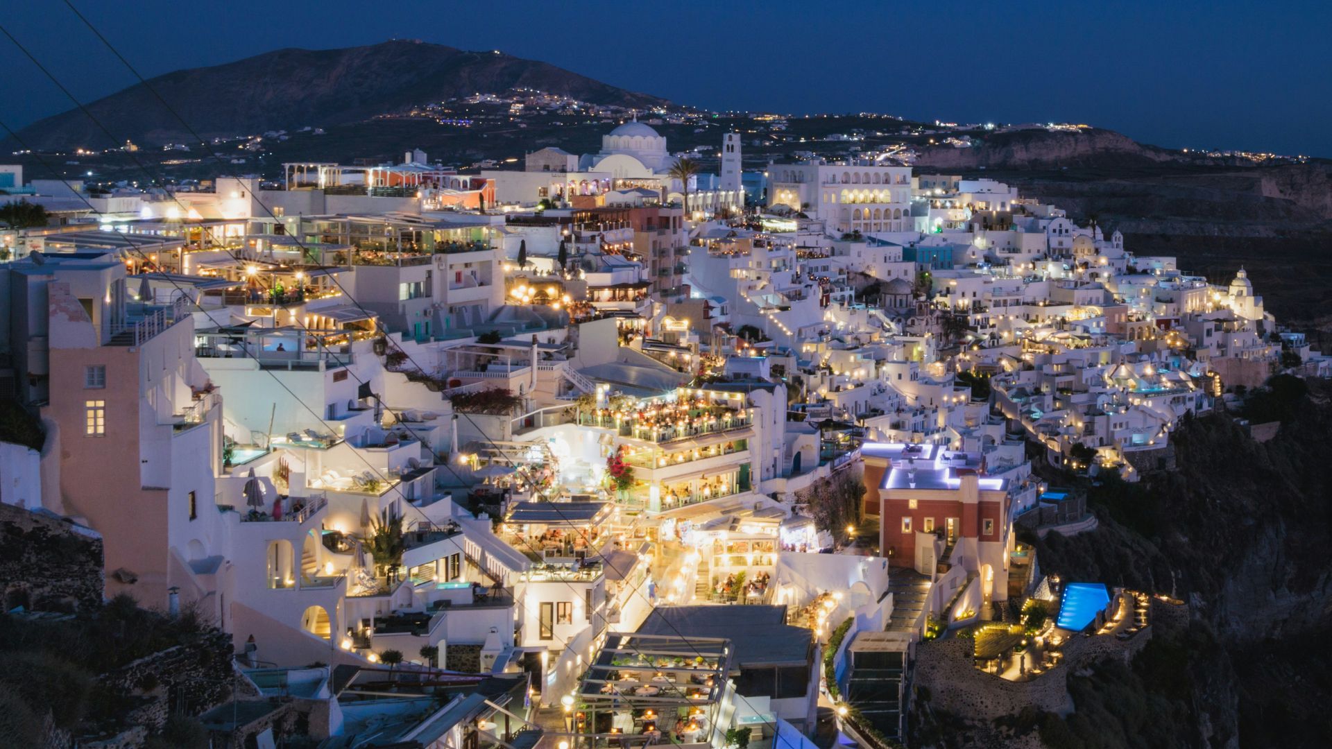Night view of Fira, Santorini, with illuminated white buildings and a dark sky.